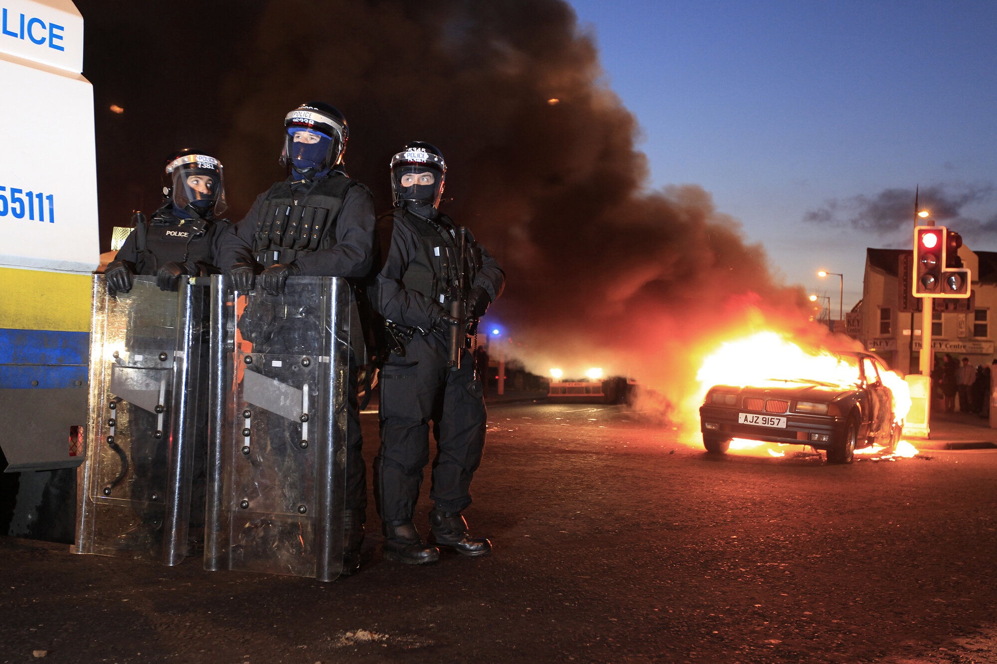 Members of the PSNI stand beside a burning car following riots in Belfast, 2013.