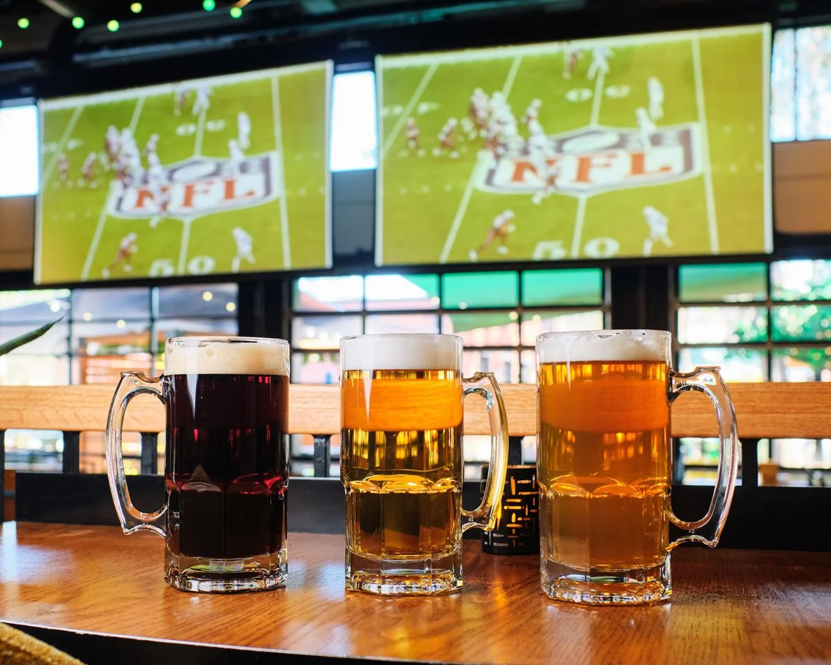 Three beers on a table in front of screens showing football. Photo credit: Brandon Amato - www.brandonjohnamato.com