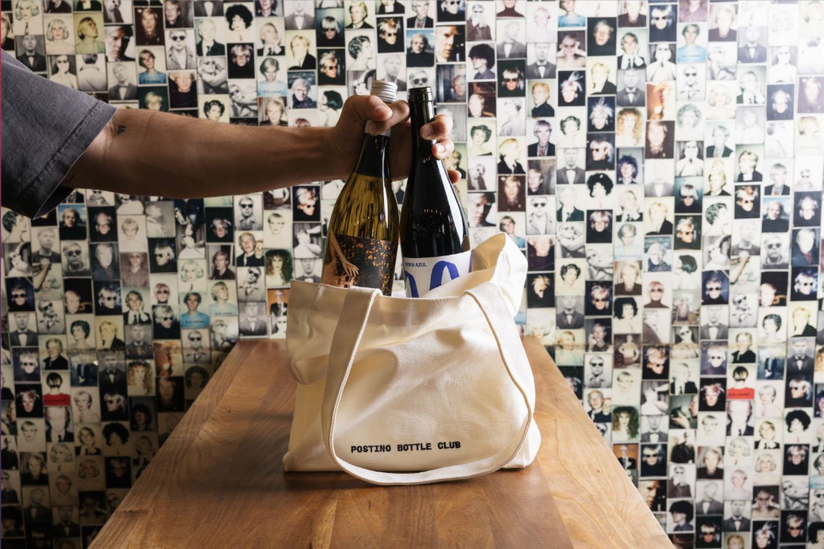 A hand holding a couple of wine bottles in a bag at Postino