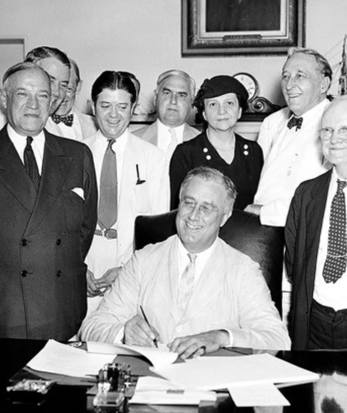 Frances Perkins stands behind President Franklin Roosevelt as he signs the Social Security Act into law on August 14, 1935.