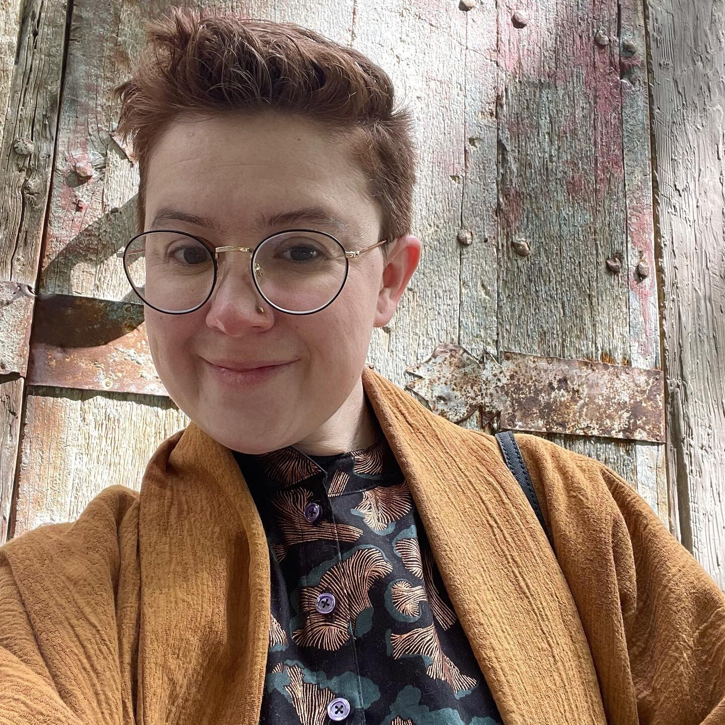 Awkward on-the-way-out selfie to show off this PRINT. 🍄
.
.
.
{Description: Lizzy, a white person with glasses and short messy hair, smiles in front of a wooden door. She is wearing a grandpa collar shirt with a print of chanterelle mushrooms in bla