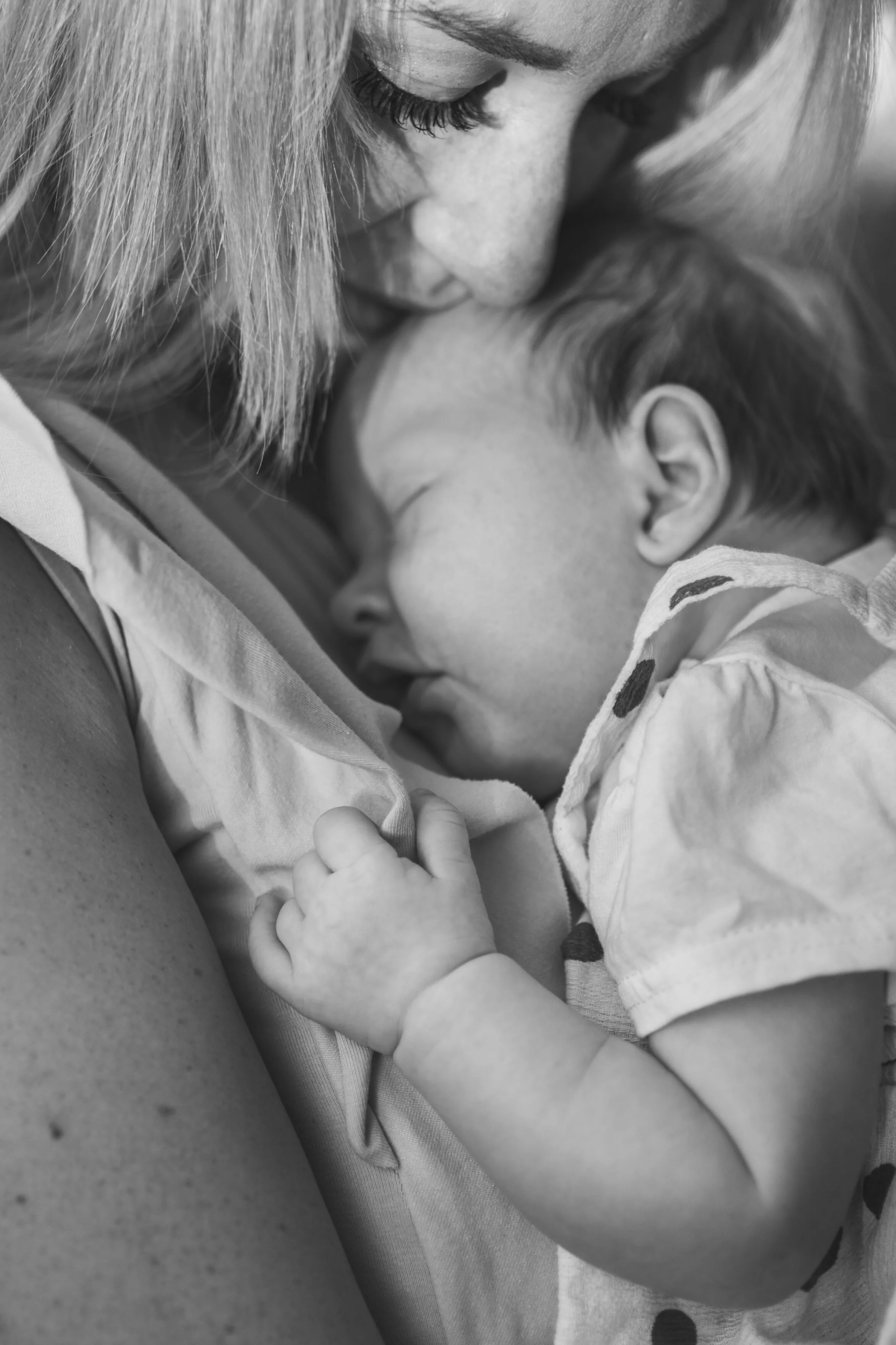 Black and white photo of a woman holding a sleeping young child close to her chest, with her face gently resting on his head.