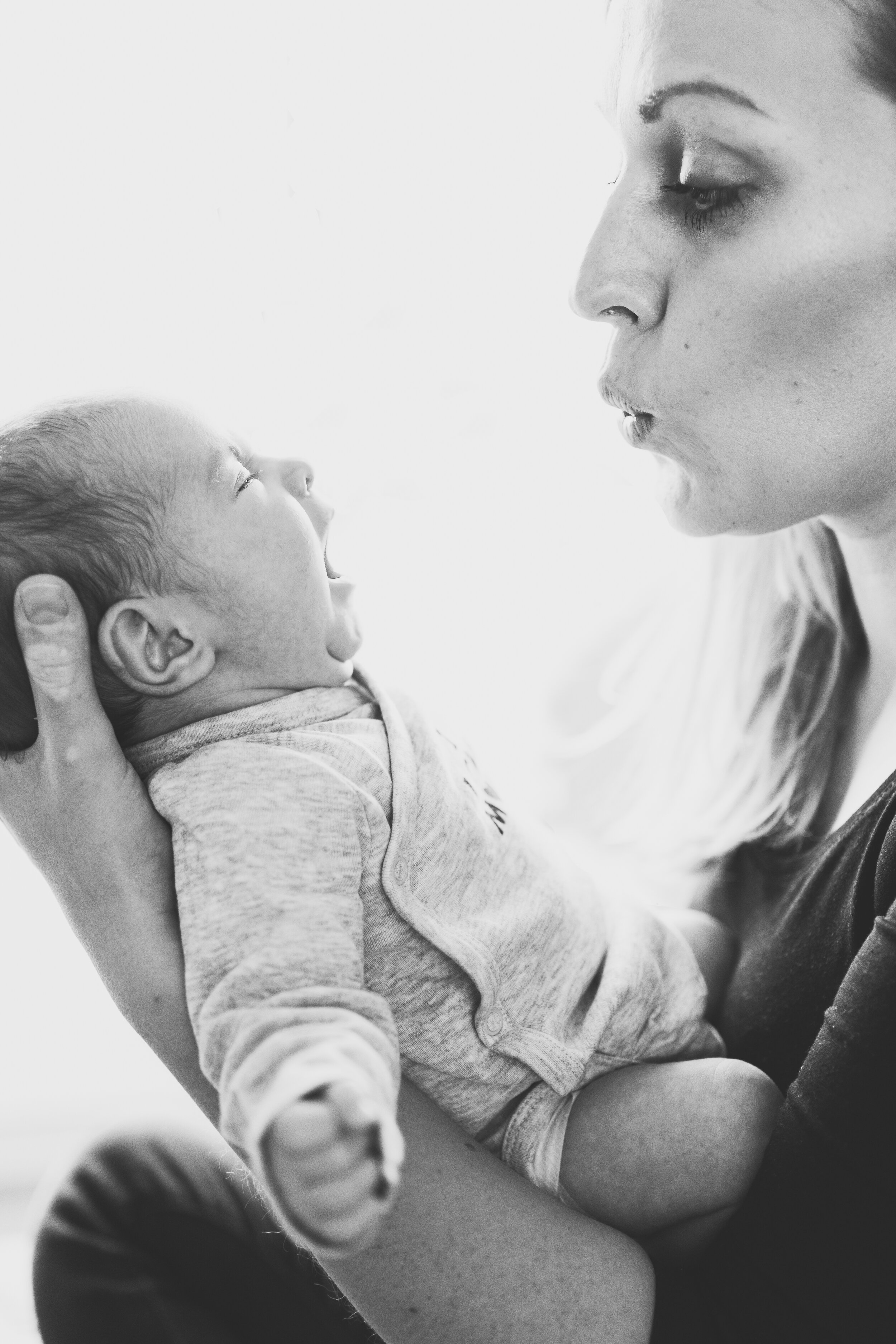 A woman holding a baby close to her face, both captured in profile. The baby appears to be yawning or making a sound, and the woman is looking at the baby.