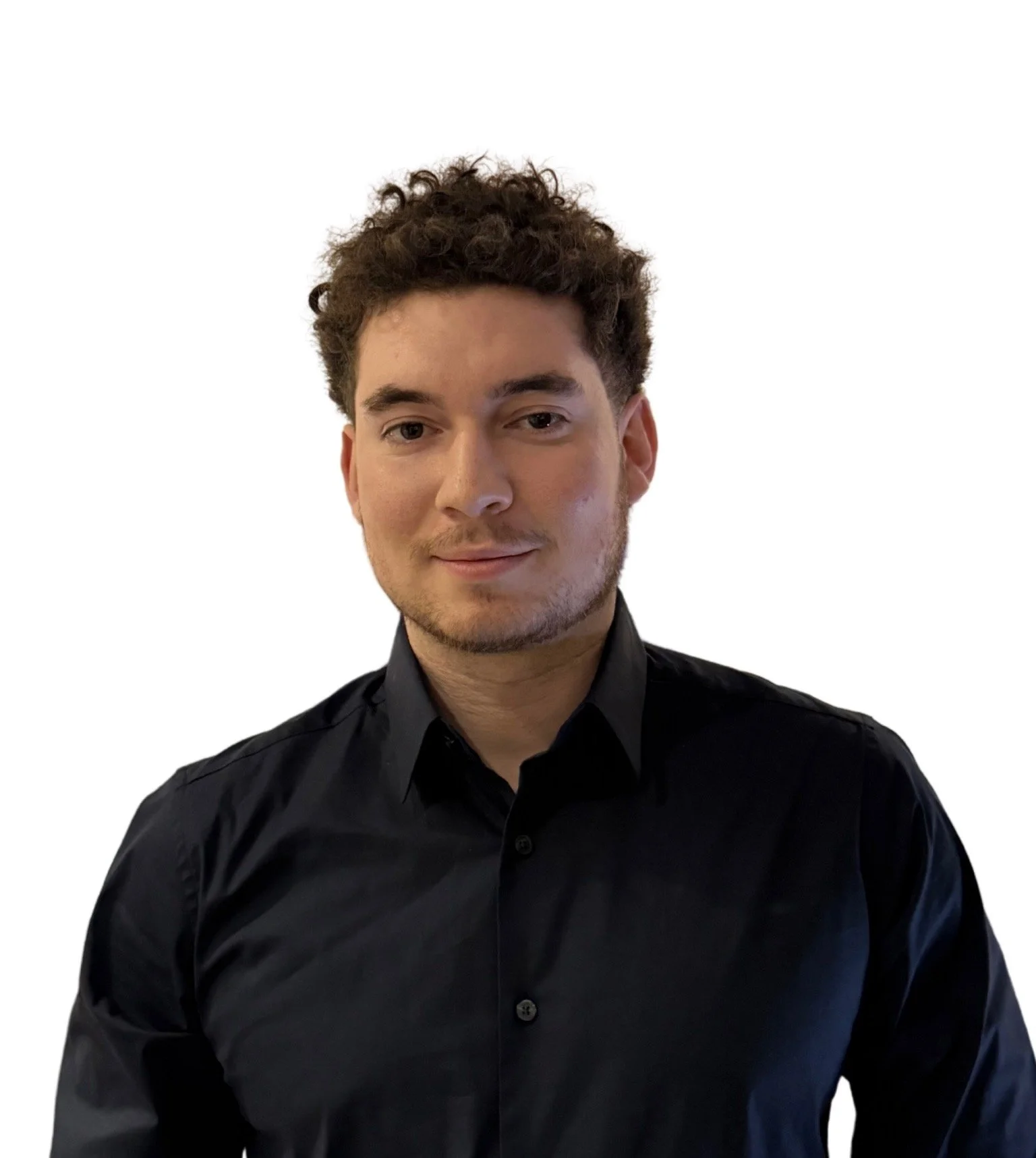 A young man with curly brown hair, light skin, wearing a black button-up shirt, facing slightly to the right and smiling softly against a white background.