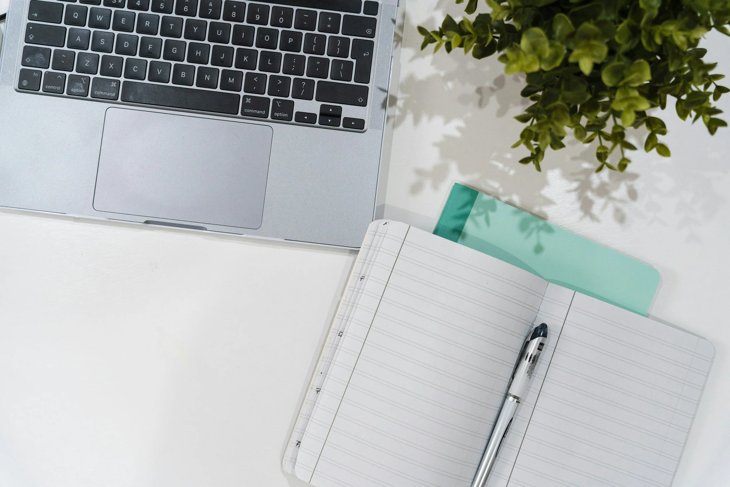 Notebook with pen, laptop on desk