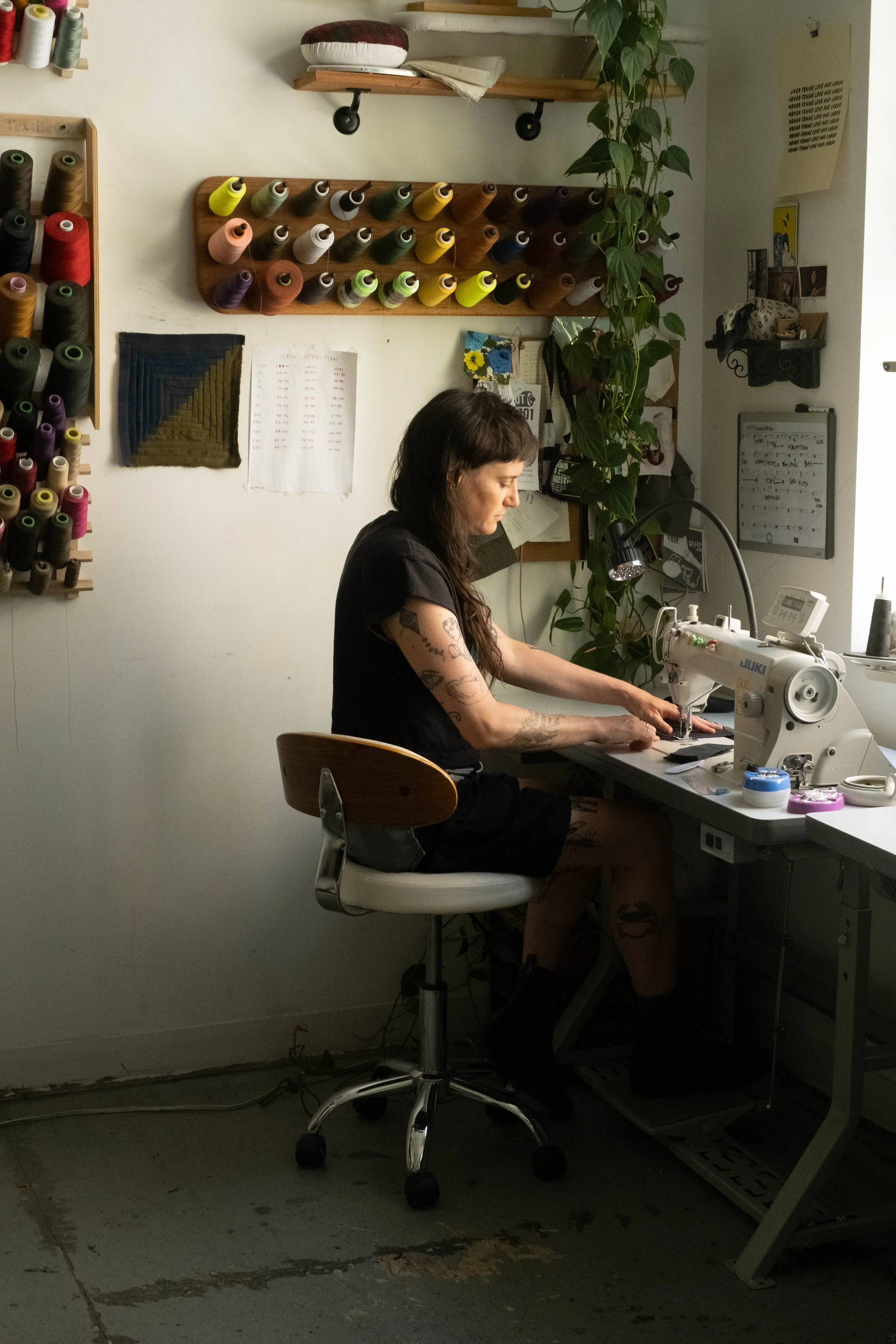 siobhan sews with a warm soft afternoon light, racked thread on the wall next to them