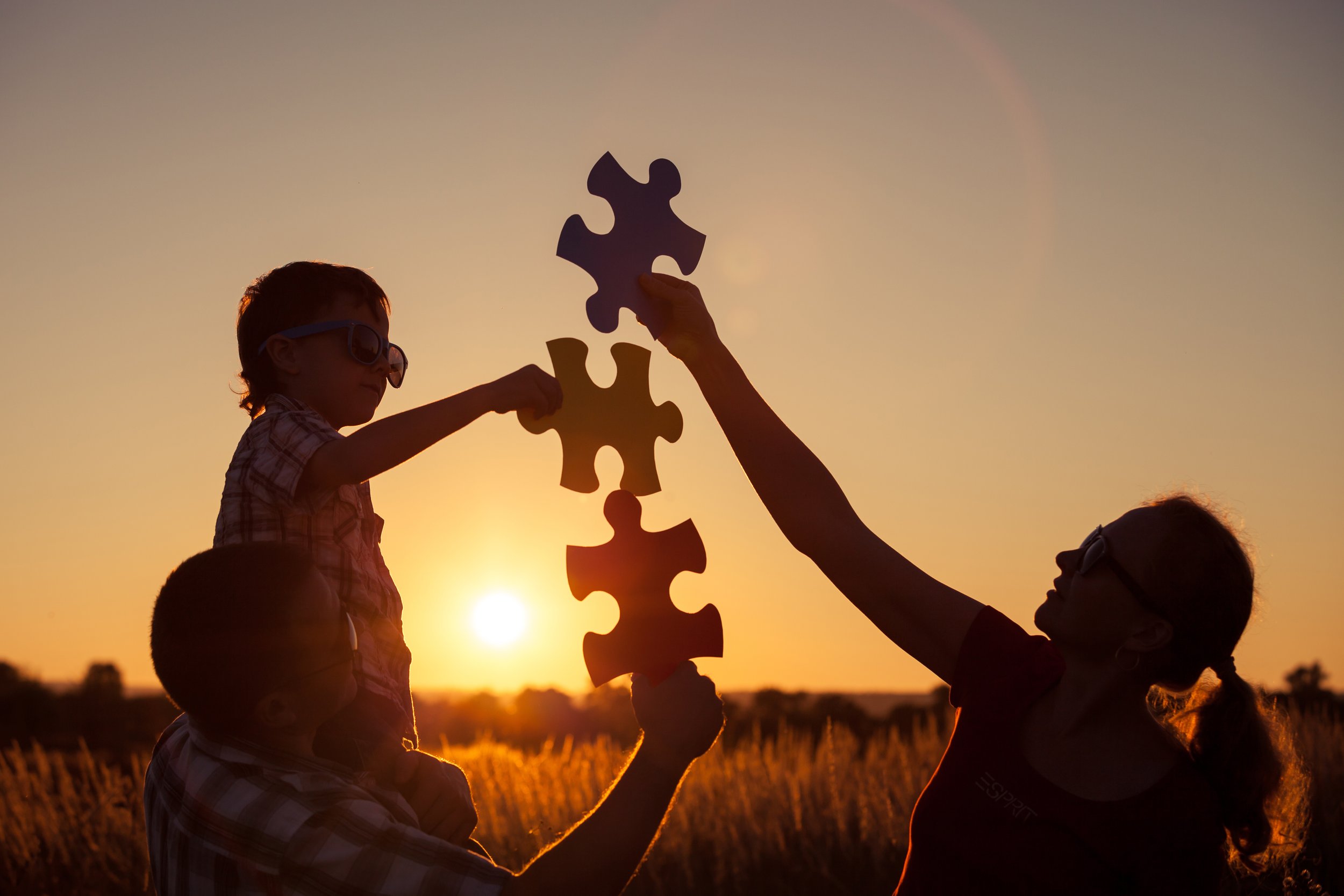 Family working together to build large puzzle pieces at sunset, symbolizing collaboration, growth, and support in a child’s communication journey.