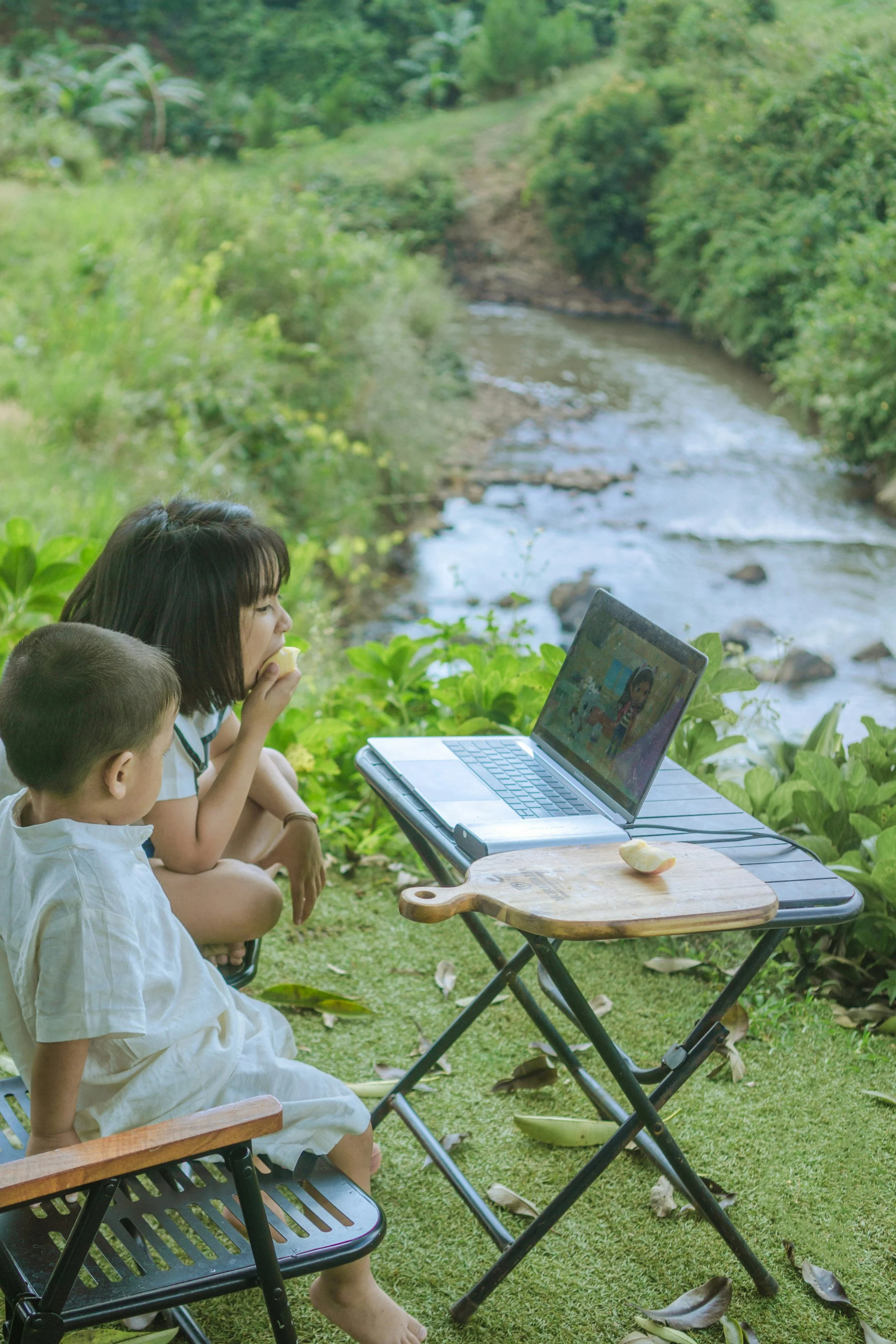 children working together on computer outside by river summer virtual learning