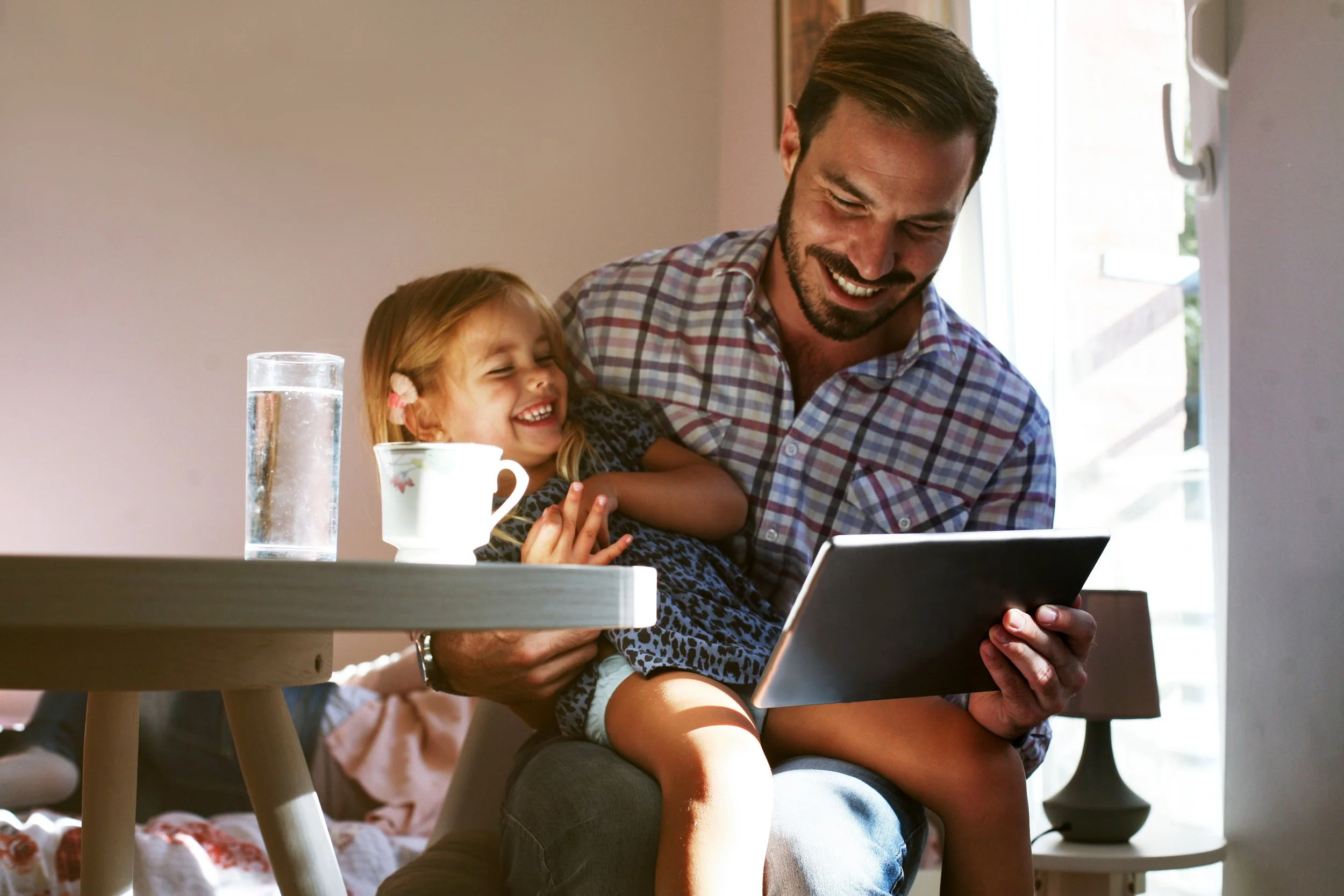 Parent and child smiling together during an online speech therapy session using a tablet at home.