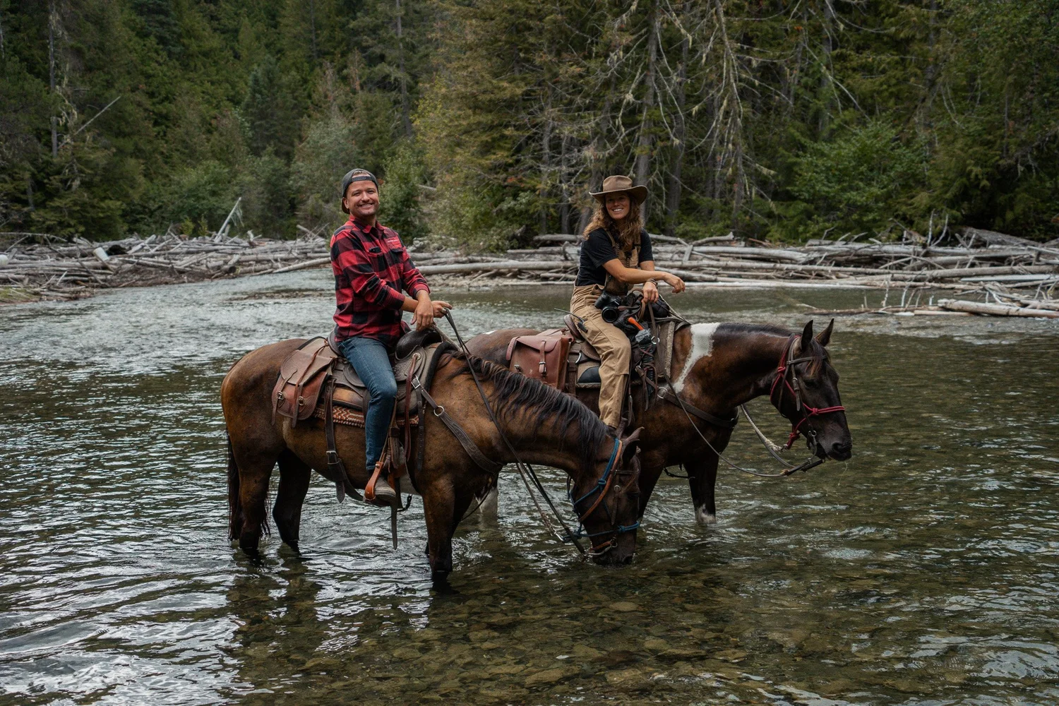 Two riders crossing a river on horseback in the Pemberton backcountry