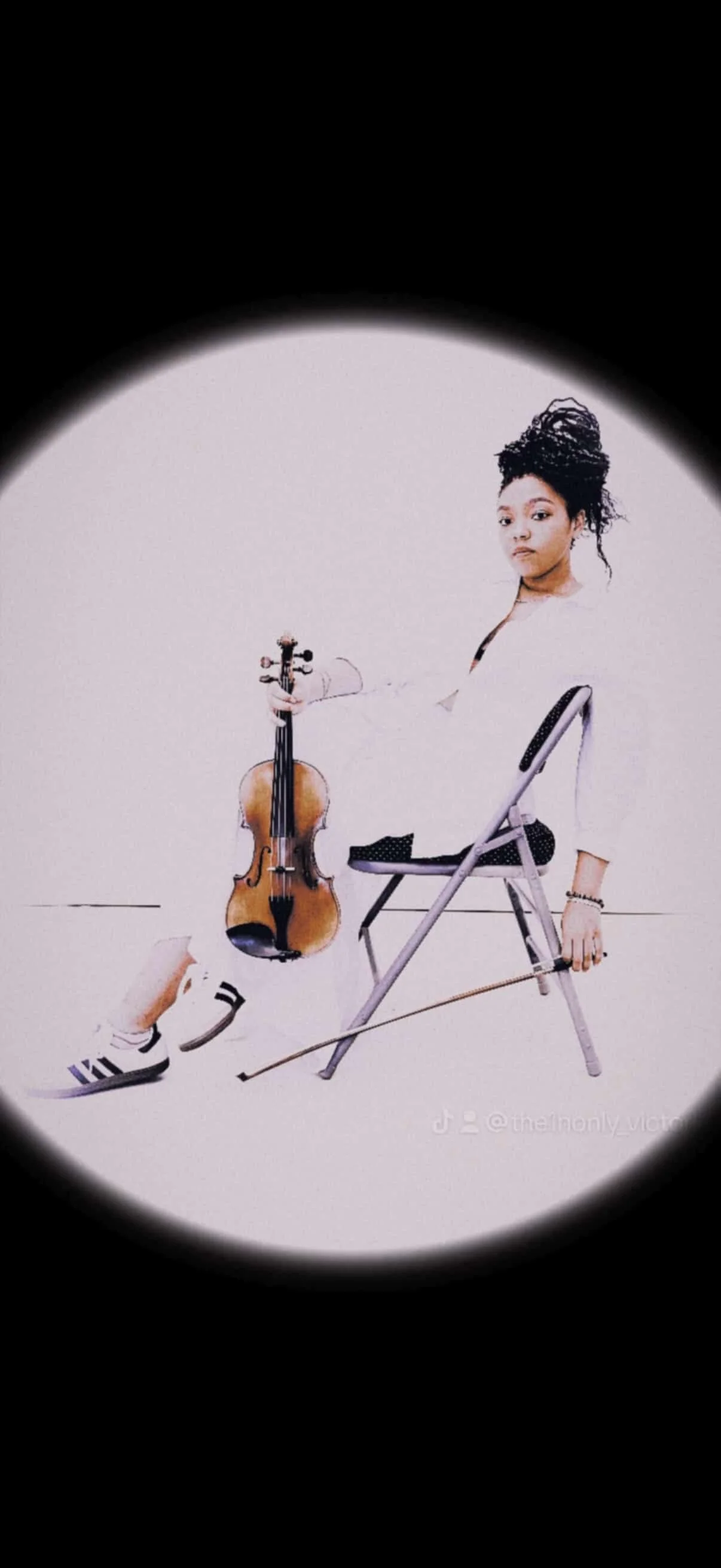 A woman sitting on a chair, holding a violin in one hand and a bow in the other, with a blank background.