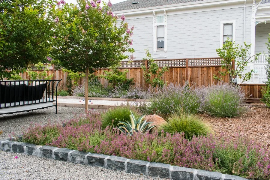 Mediterranean garden design featuring pea gravel, granite pavers, an outdoor daybed, lavender, grape myrtle, bougainvillea, and drought-tolerant plantings.
