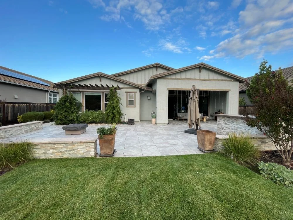 Residential landscape design featuring a patio with seating walls and an outdoor kitchen in stone pavers