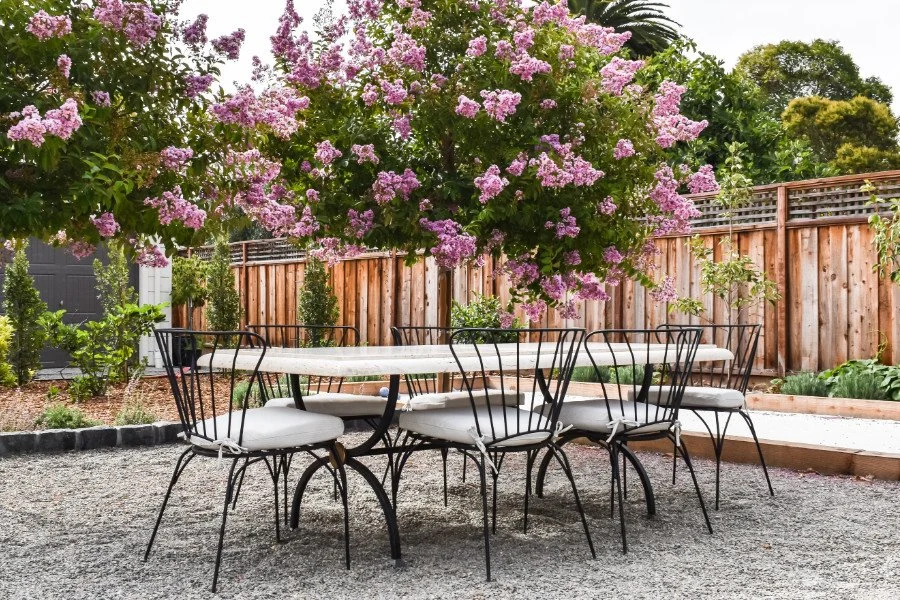 Travertine stone table with chairs on a gravel patio, surrounded by lavender grape myrtle trees