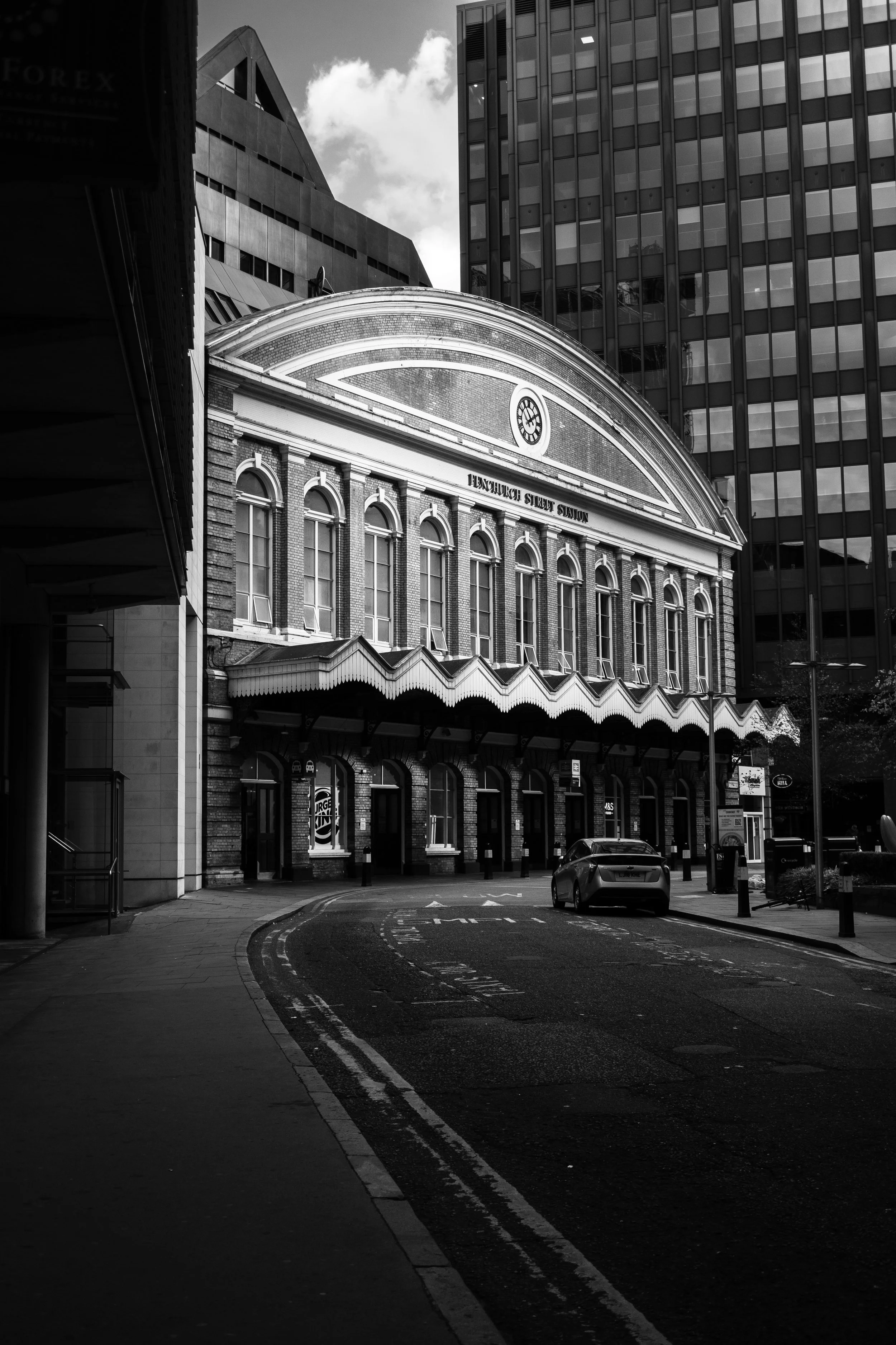 Black and white photo of Flinders Street Station with a curved street and modern buildings in the background.