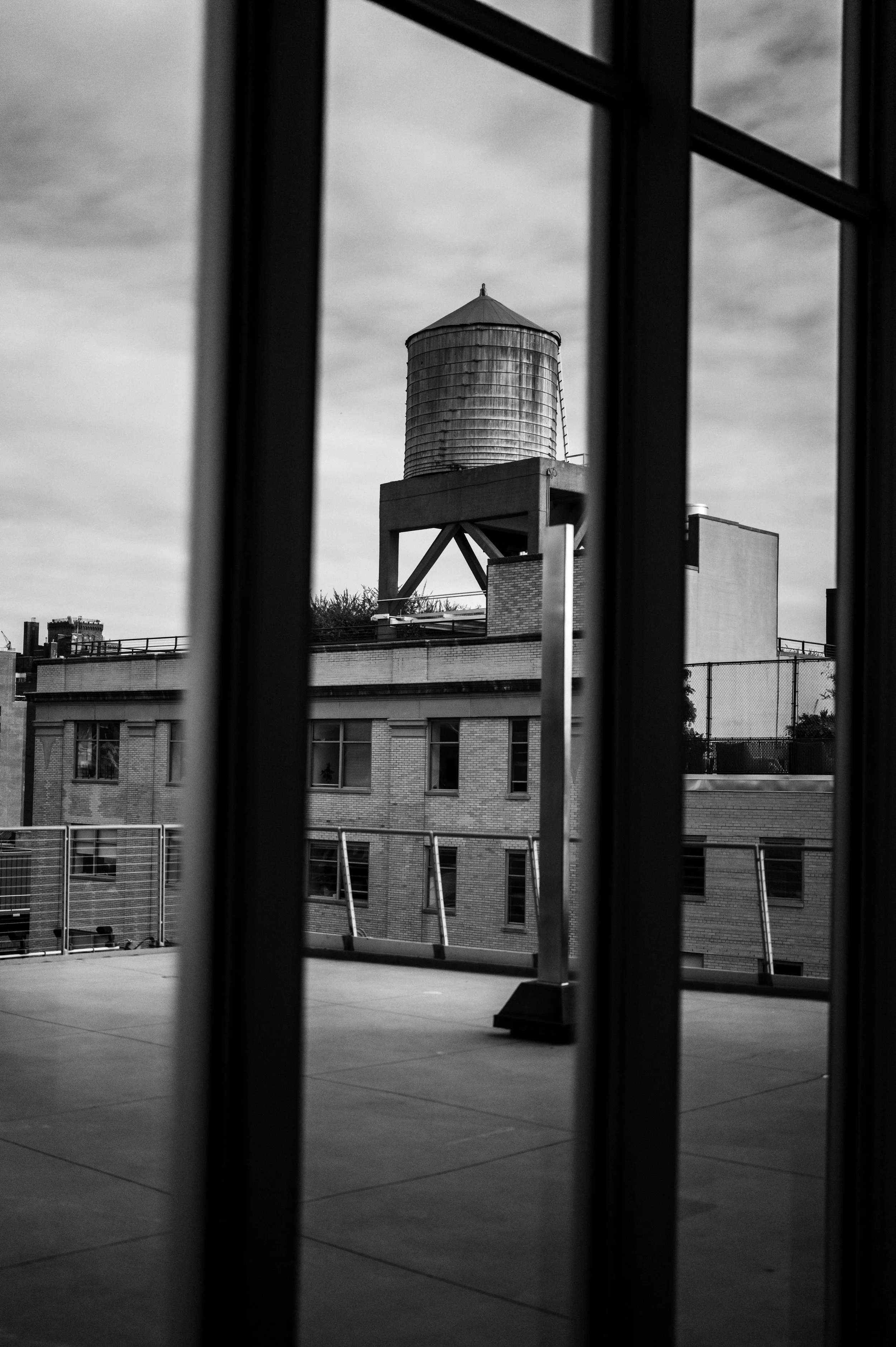 View of a building with a water tower seen through vertical bars, black and white photograph.
