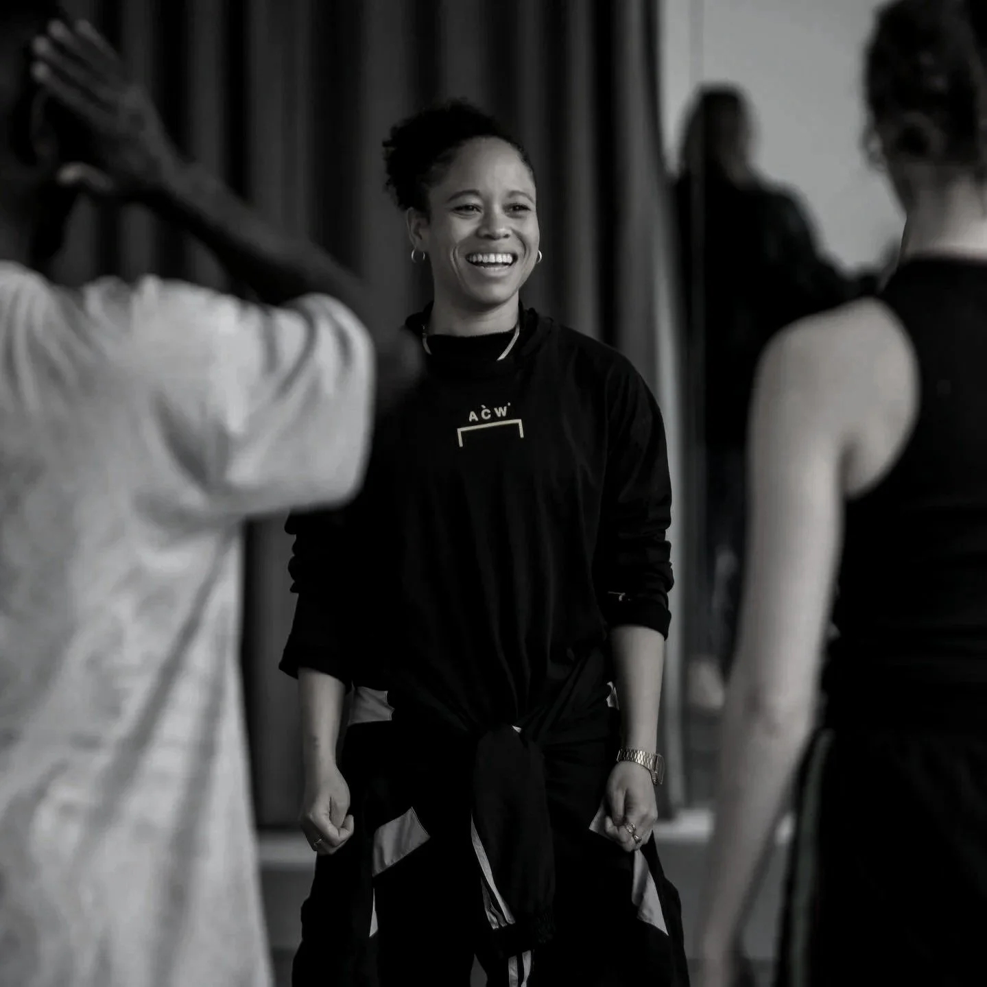 A woman smiling and looking at another person, surrounded by others in a social or professional setting.