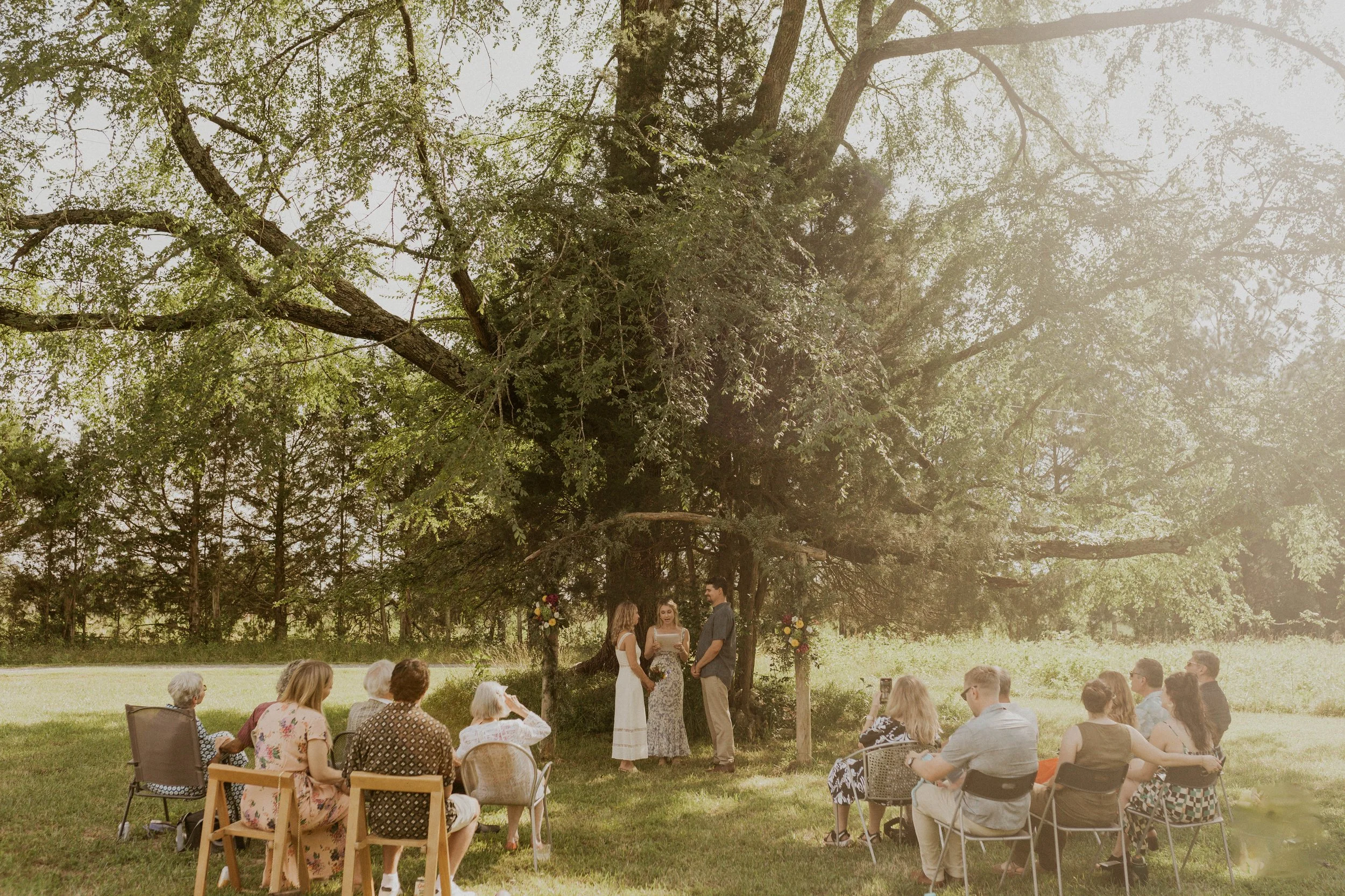 Intimate elopement ceremony under a large tree in a wildflower-filled field