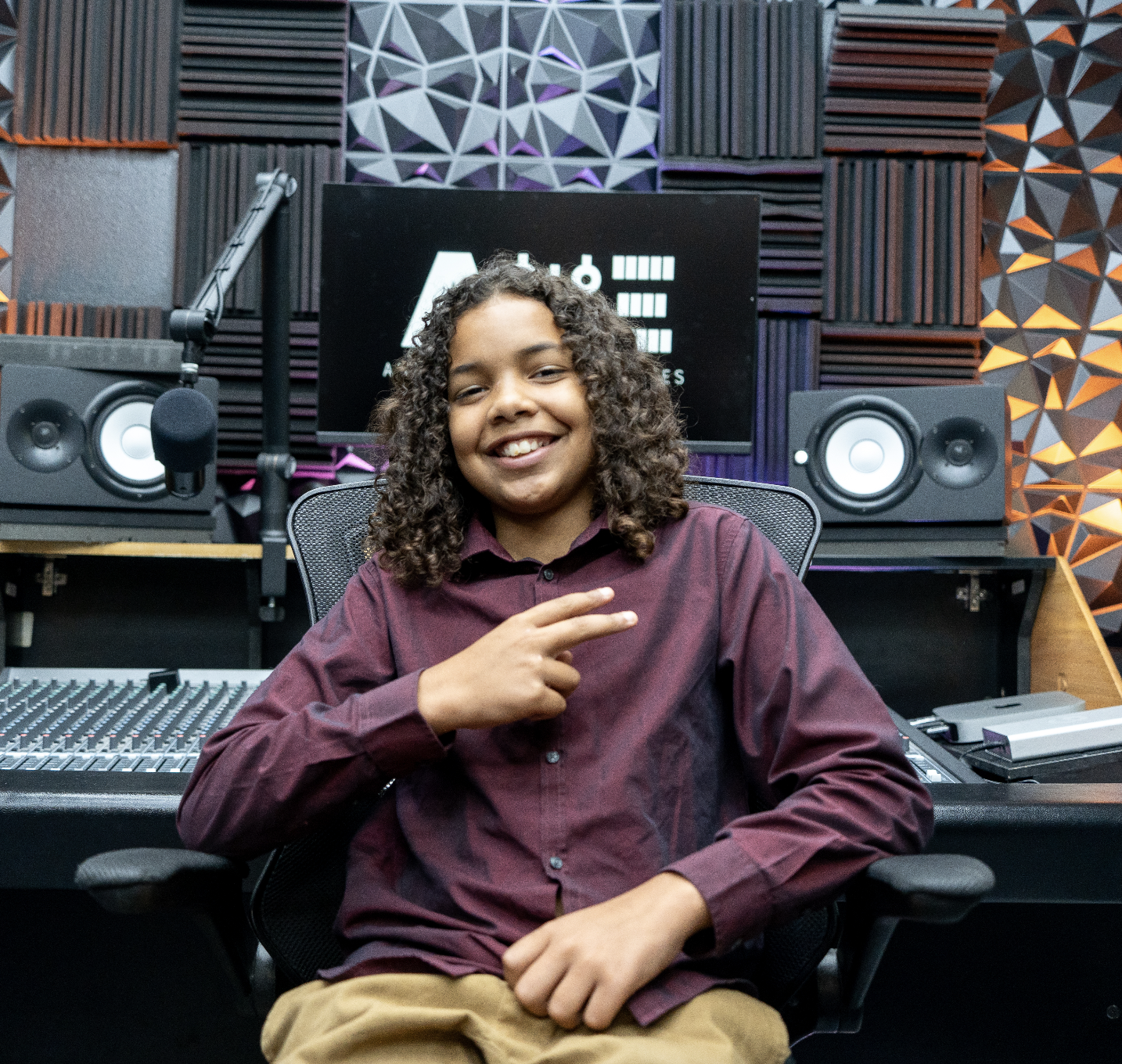 An aspiring creative professional in our 2024 Music House Summer Camp Cohort poses in front of the control room desk in Anthem Music Enterprises' audio production suite.