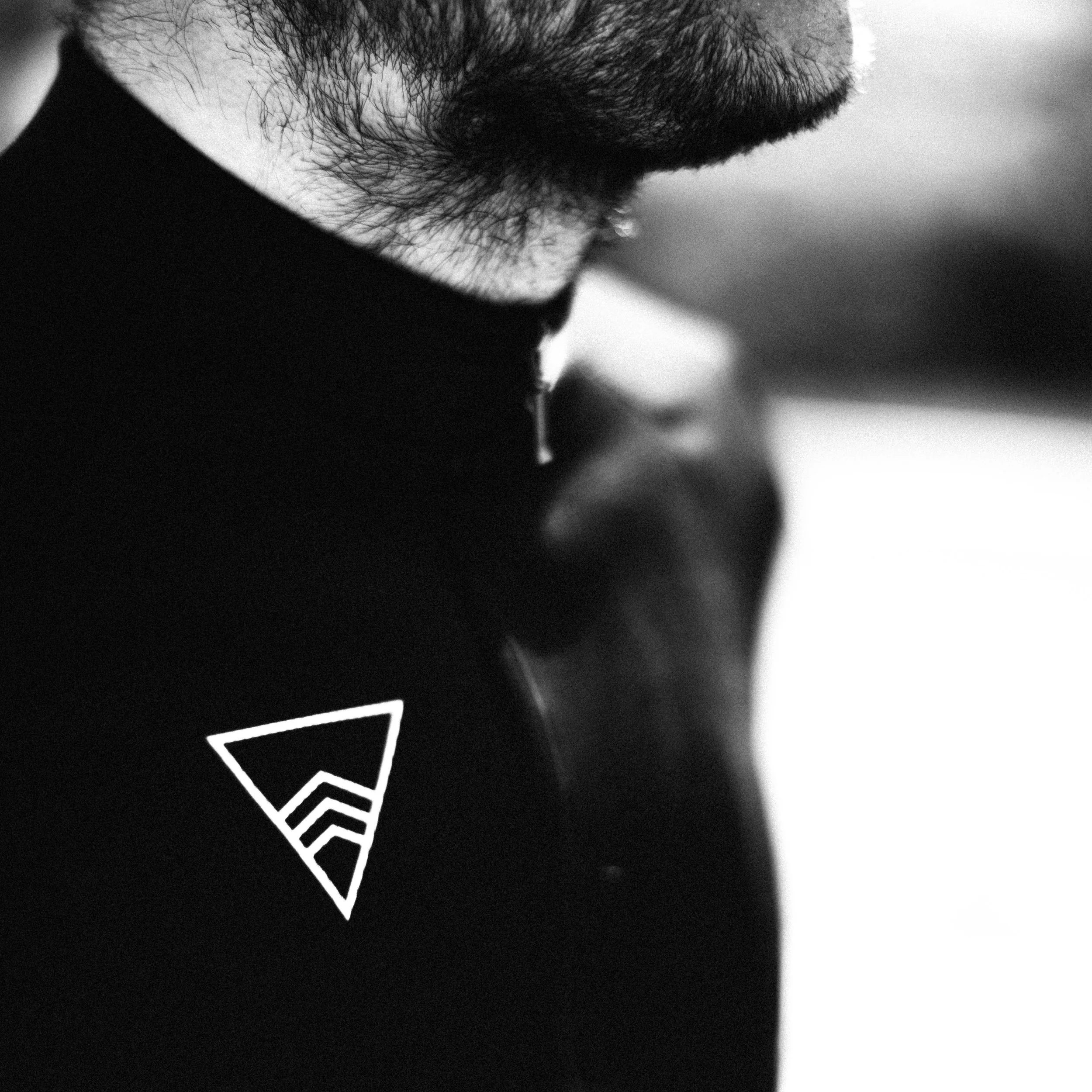 Close-up black and white photograph of a person's face focusing on the beard and part of the mouth, with a geometric design on their black shirt.