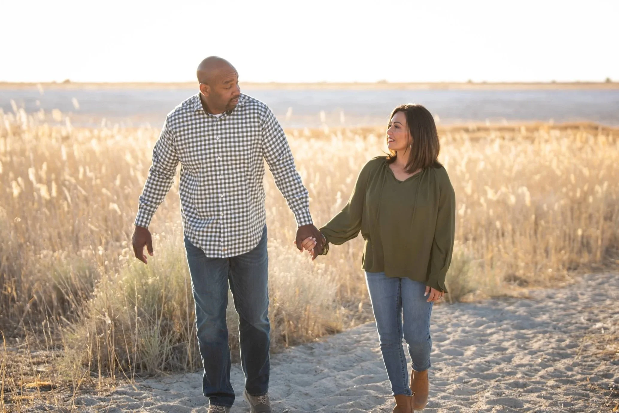 A couple walks through the tall grass in alpenglow at Antelope Island, by Gloho Photography
