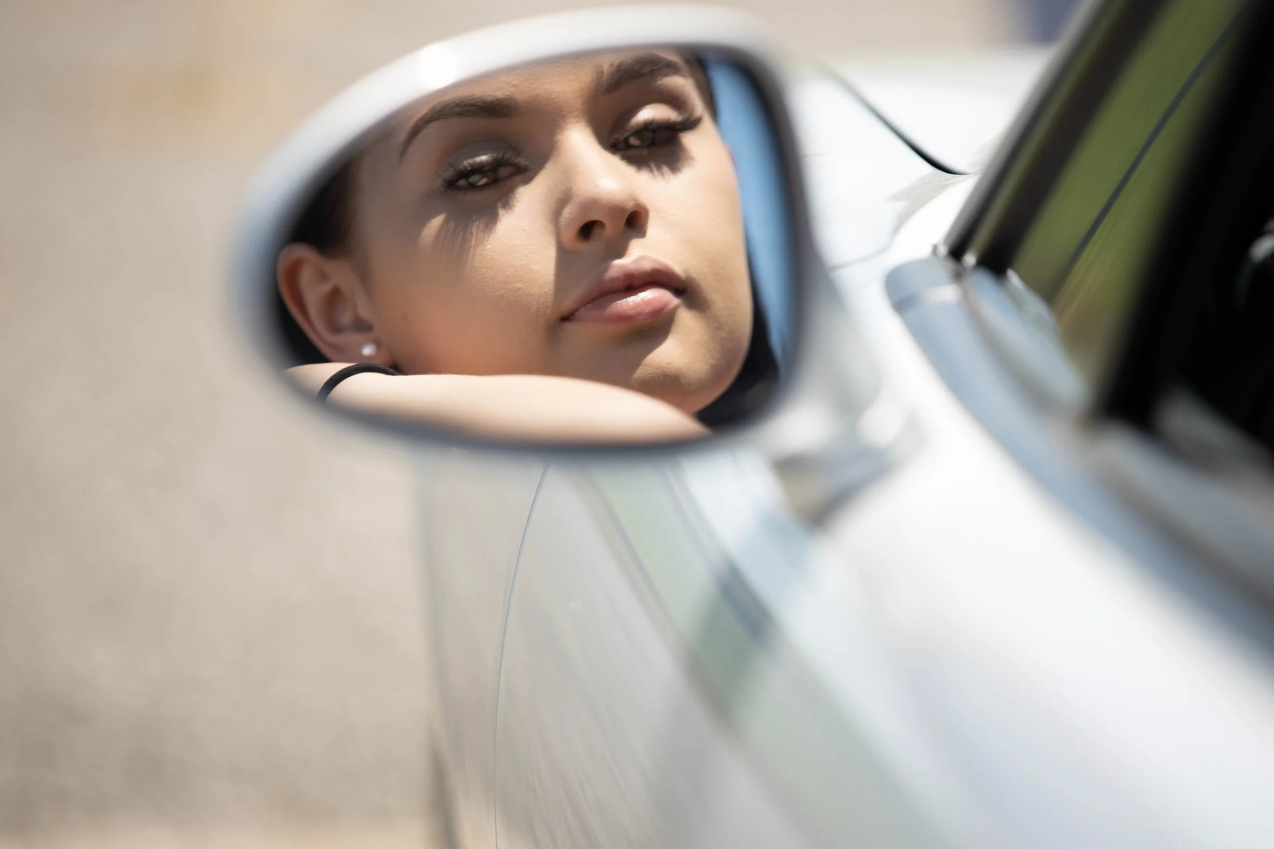 Close-up of a woman looking into a car's side mirror with her arm resting on the car door. Graduation photography by Digital Imageries Photography.