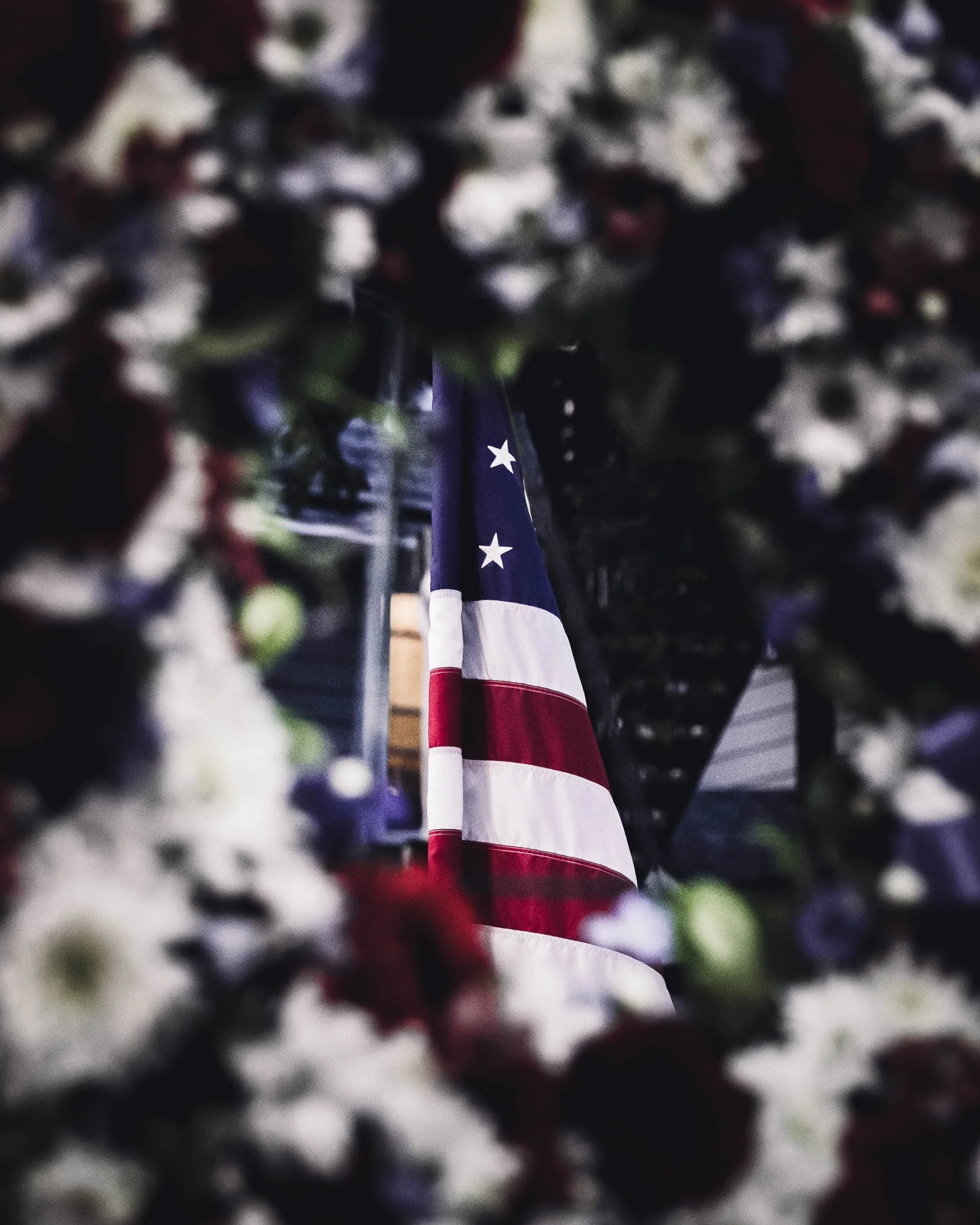 American flag draped on a wall, viewed through a frame of blurred white and red flowers.