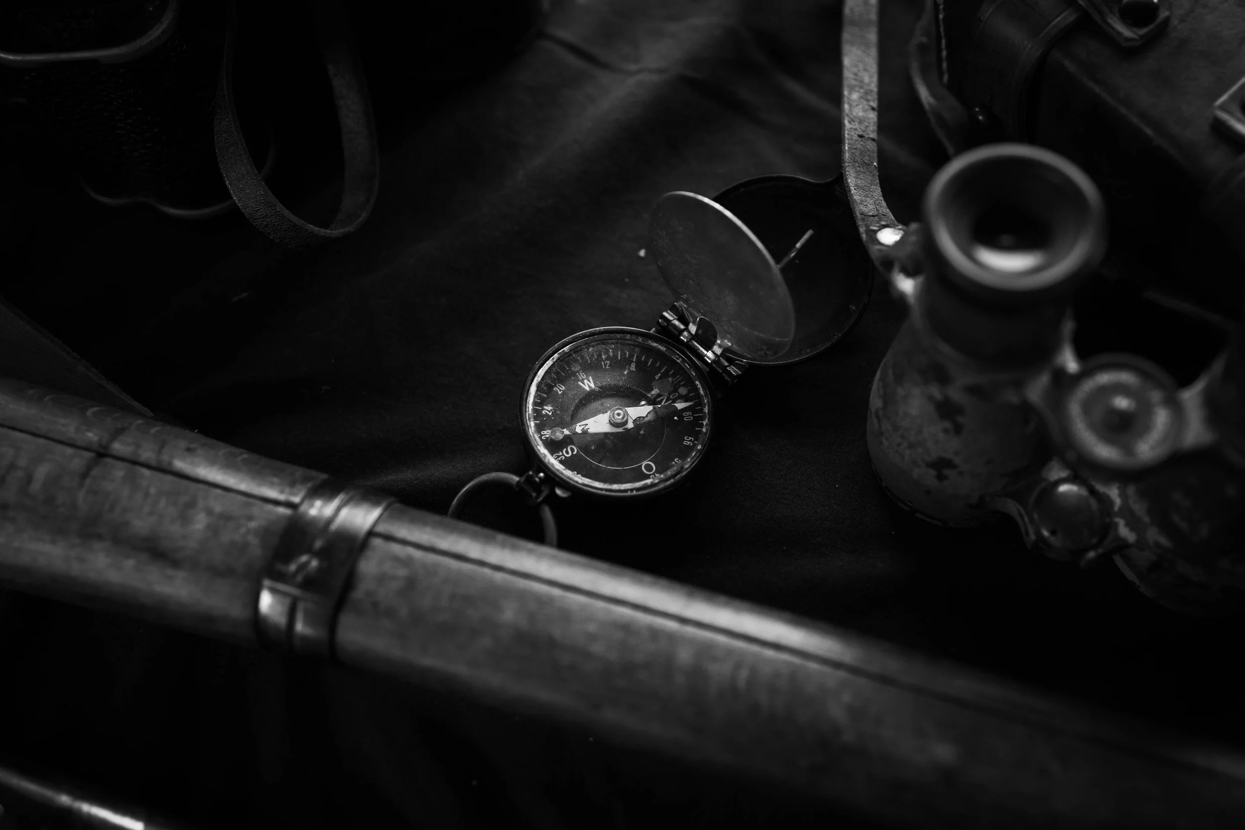 A close-up, high-contrast shot of vintage military gear, including a canteen and leather straps, laying on a dark surface.
