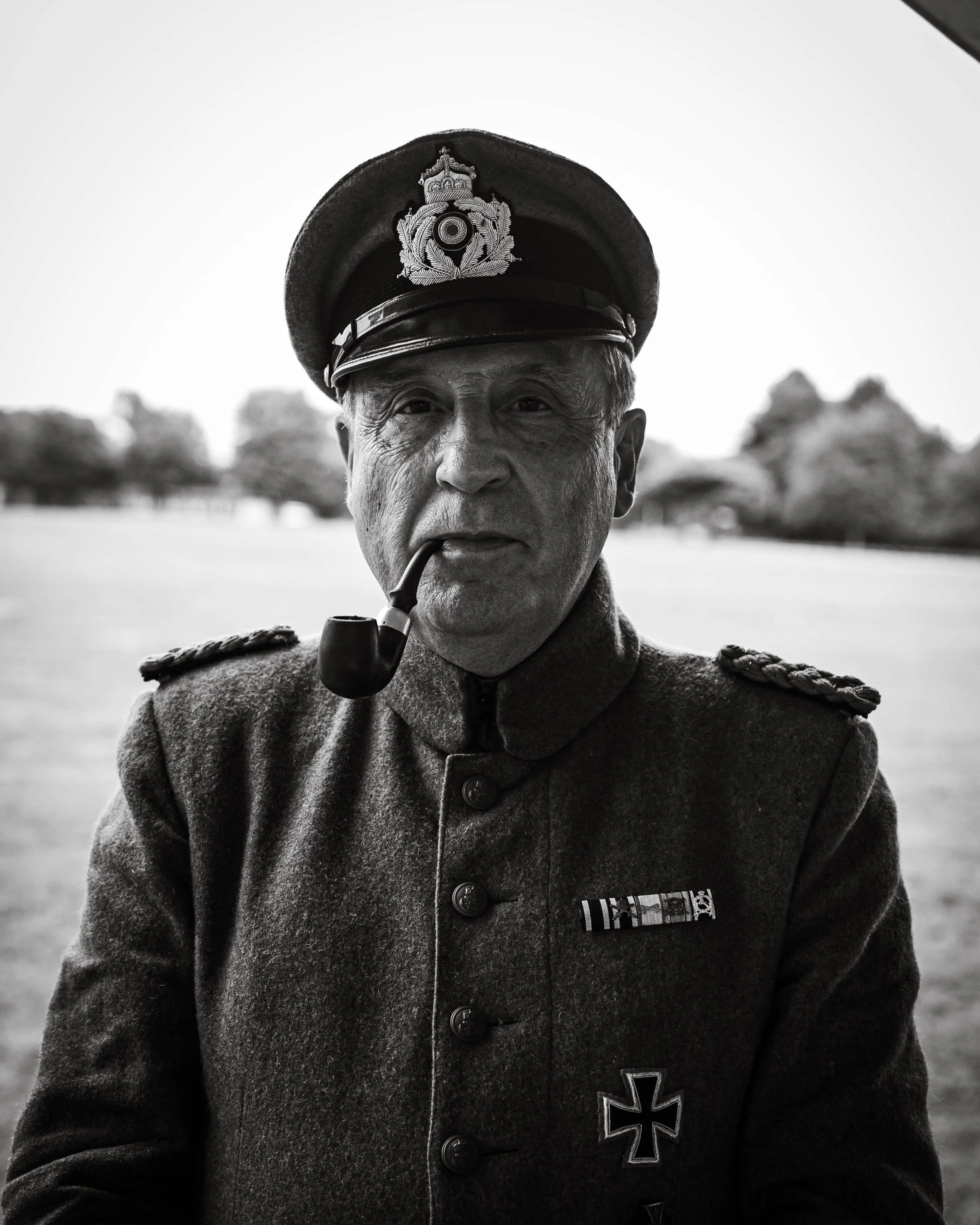 A close-up, black and white portrait of a somber officer in a formal peaked cap and dress uniform at a military memorial event.