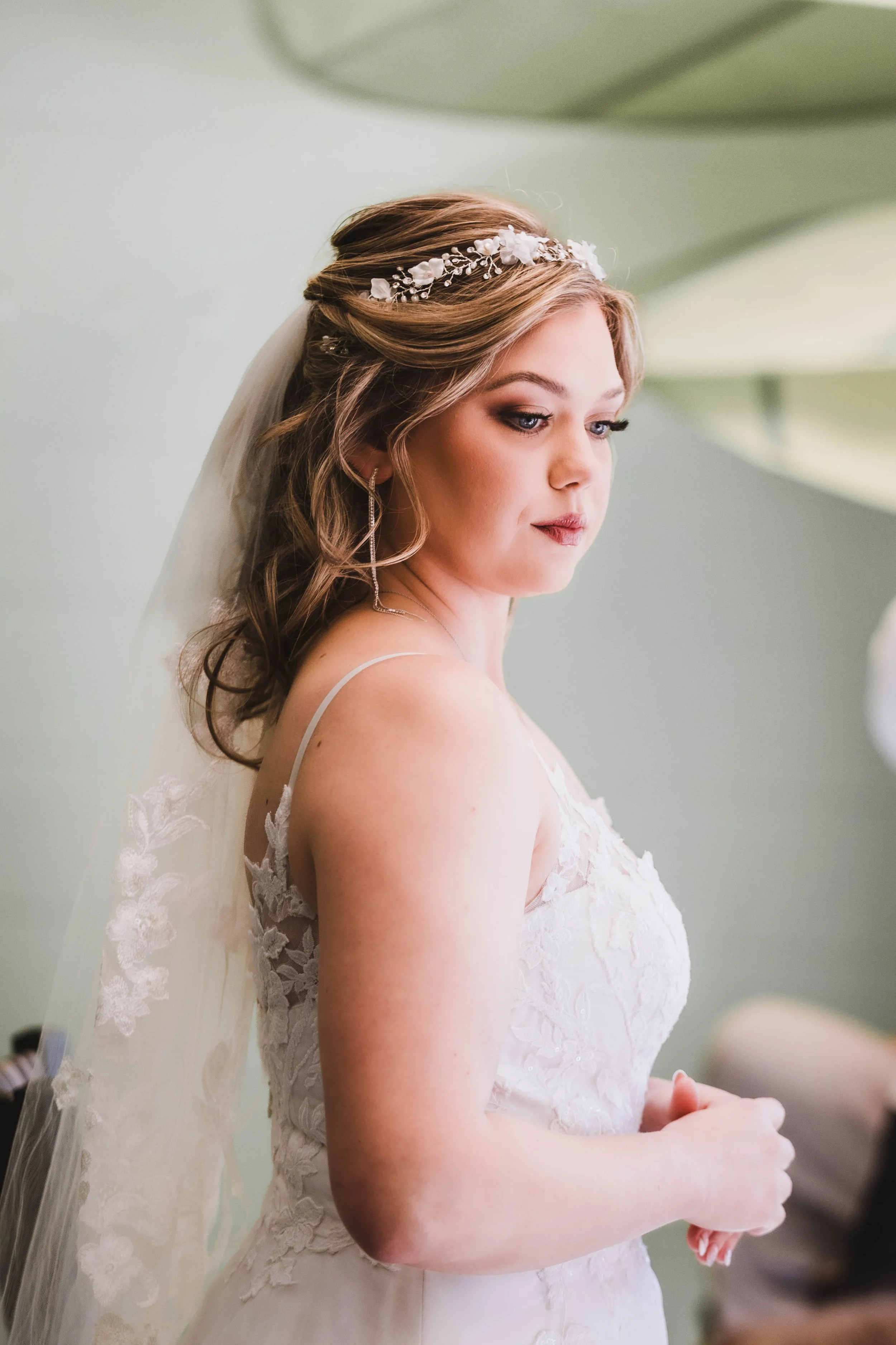 A bride in a lace wedding gown with a floral headband and veil, captured in a quiet, intimate bridal portrait moment before the ceremony.