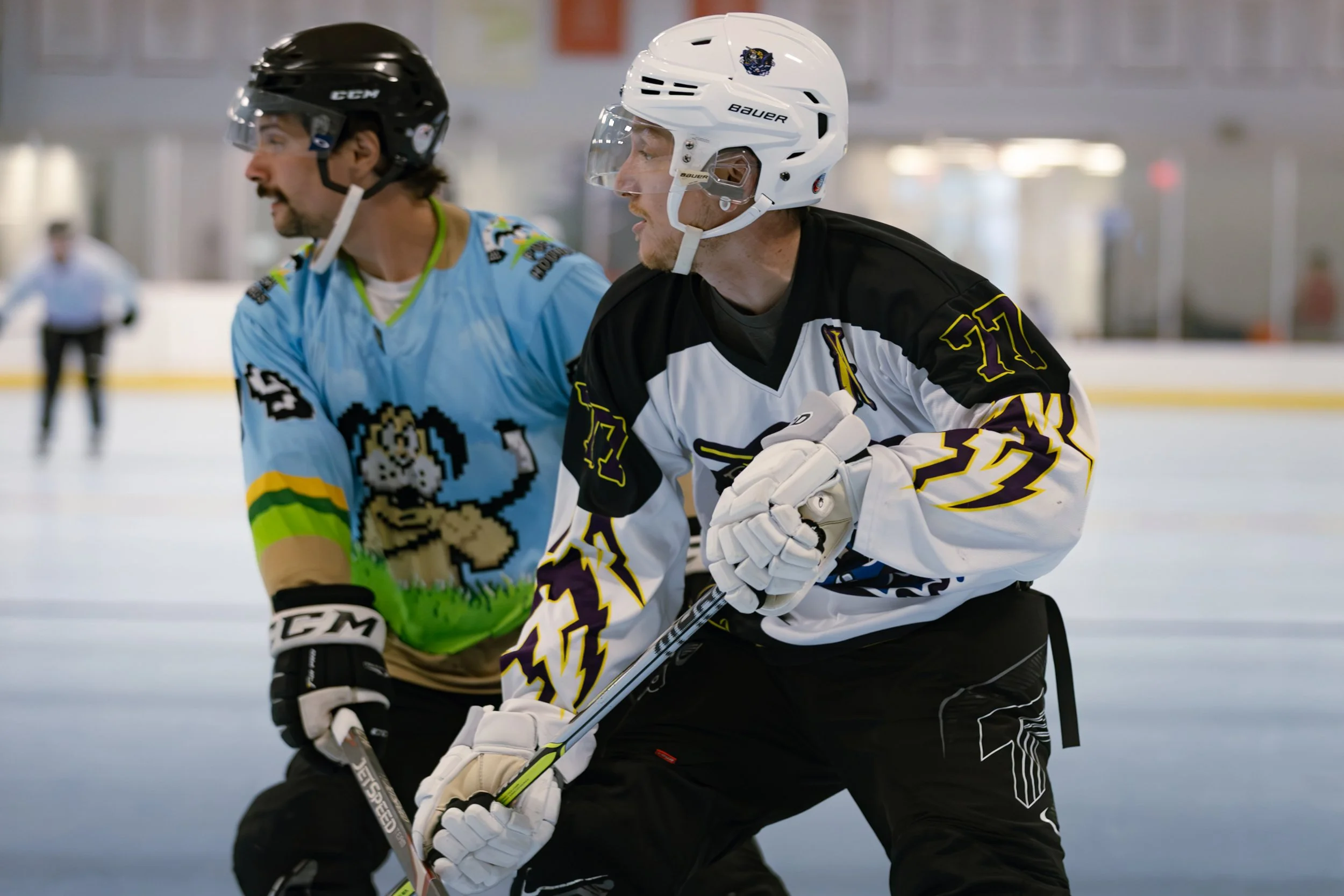 Two ice hockey players wearing helmets and jerseys skating on the ice rink during a game.