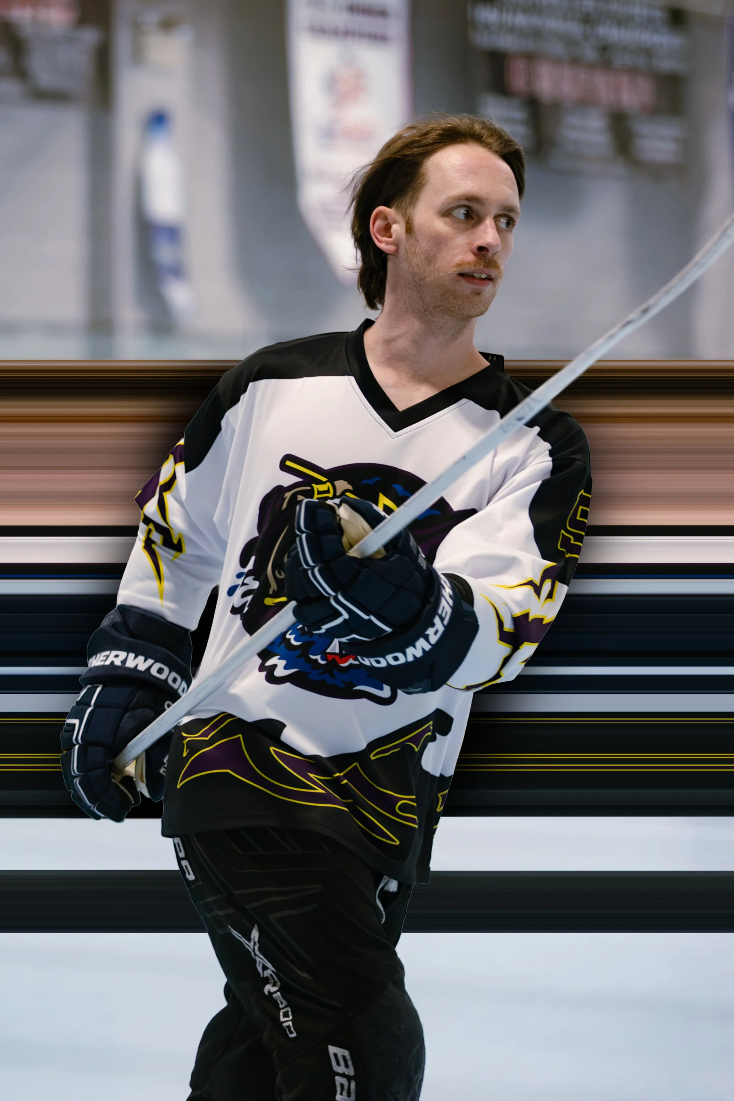 A man in a hockey jersey with a bear logo on it, holding a hockey stick, standing on an ice rink.