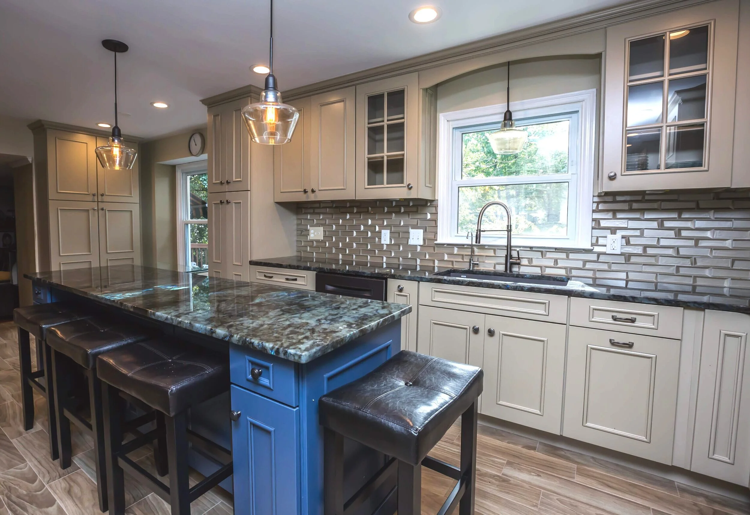 Antique lantern-style lighting over the marble bar, complete with natural light, leather seating, airy olive cabinets with glass window-work, and a modern faucet.