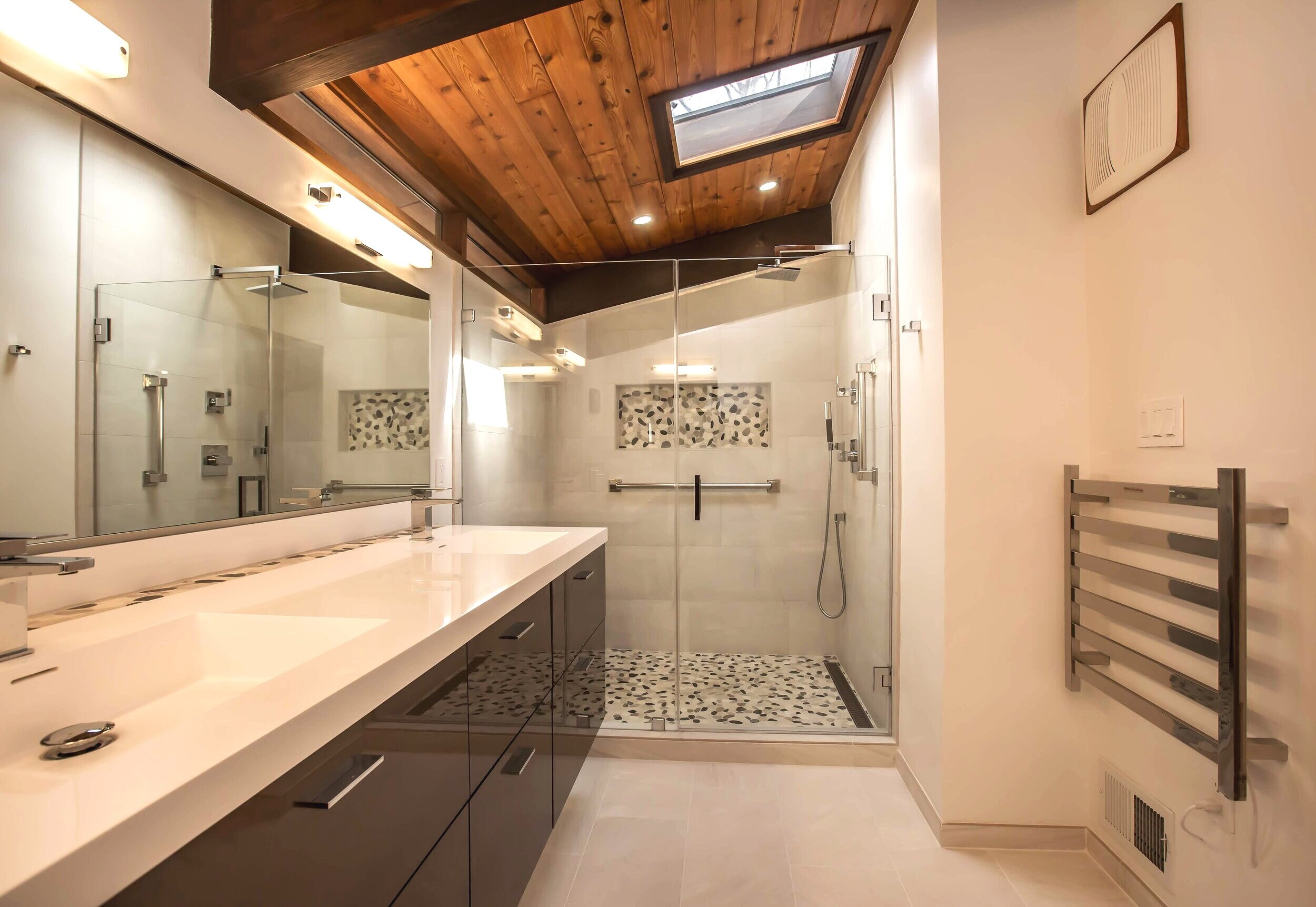 A view of the sleek shower with chrome pieces, expressionistic inlaid tile work, and stunning stone.
