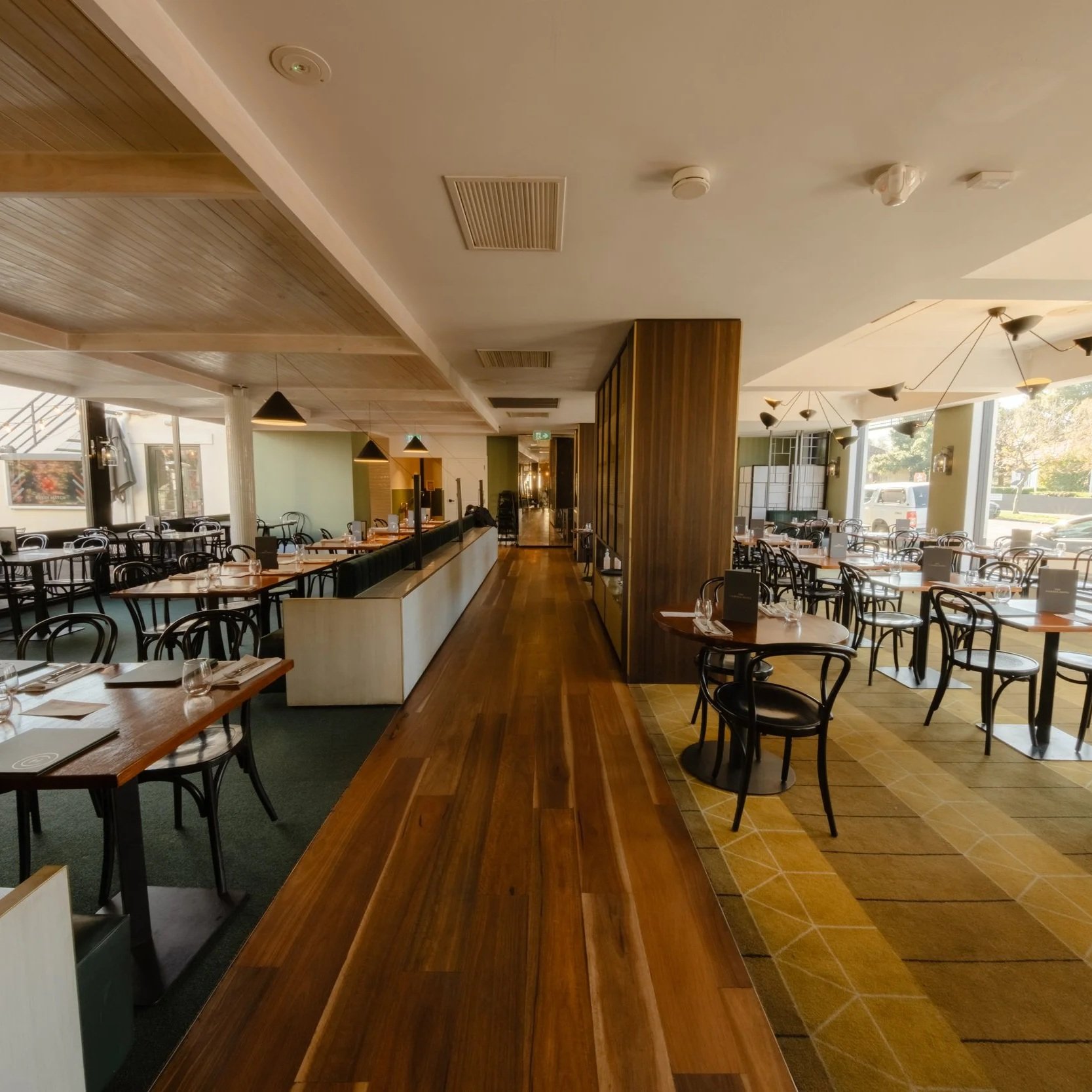 The Camden's Bistro with wooden flooring, tables set with glasses and silverware, black chairs, large windows, modern light fixtures, and a decorative wooden partition.