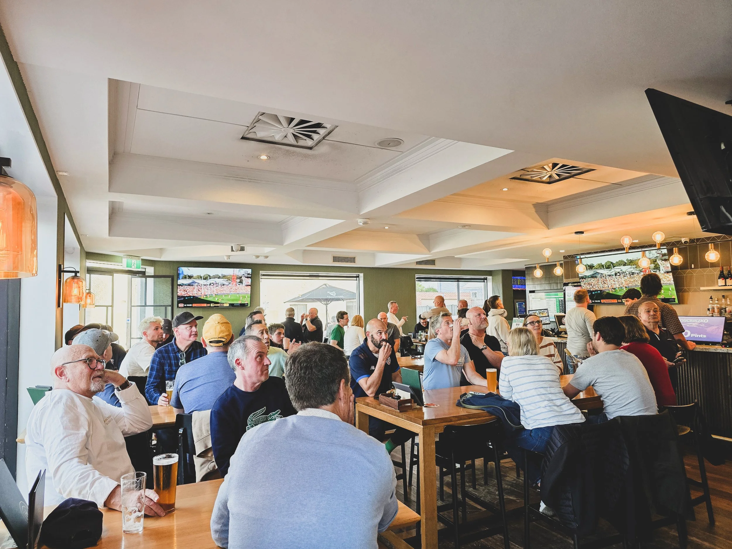 Crowd of people watching a sporting event on TVs in a restaurant or bar with a modern ceiling design and warm lighting at the Camden Hotel