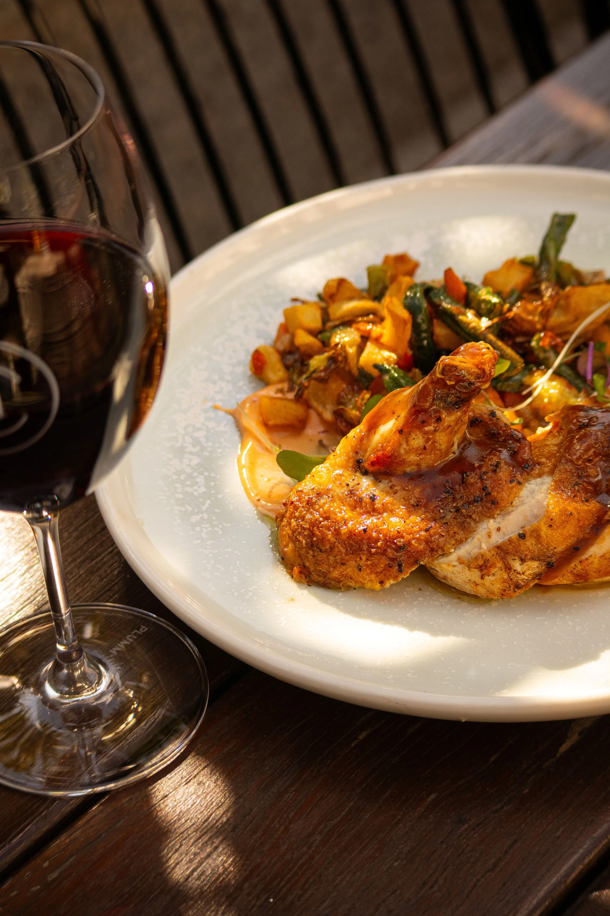 A plate with roasted chicken, served with vegetables, and a glass of red wine on a wooden table in the courtyard, Camden Hotel