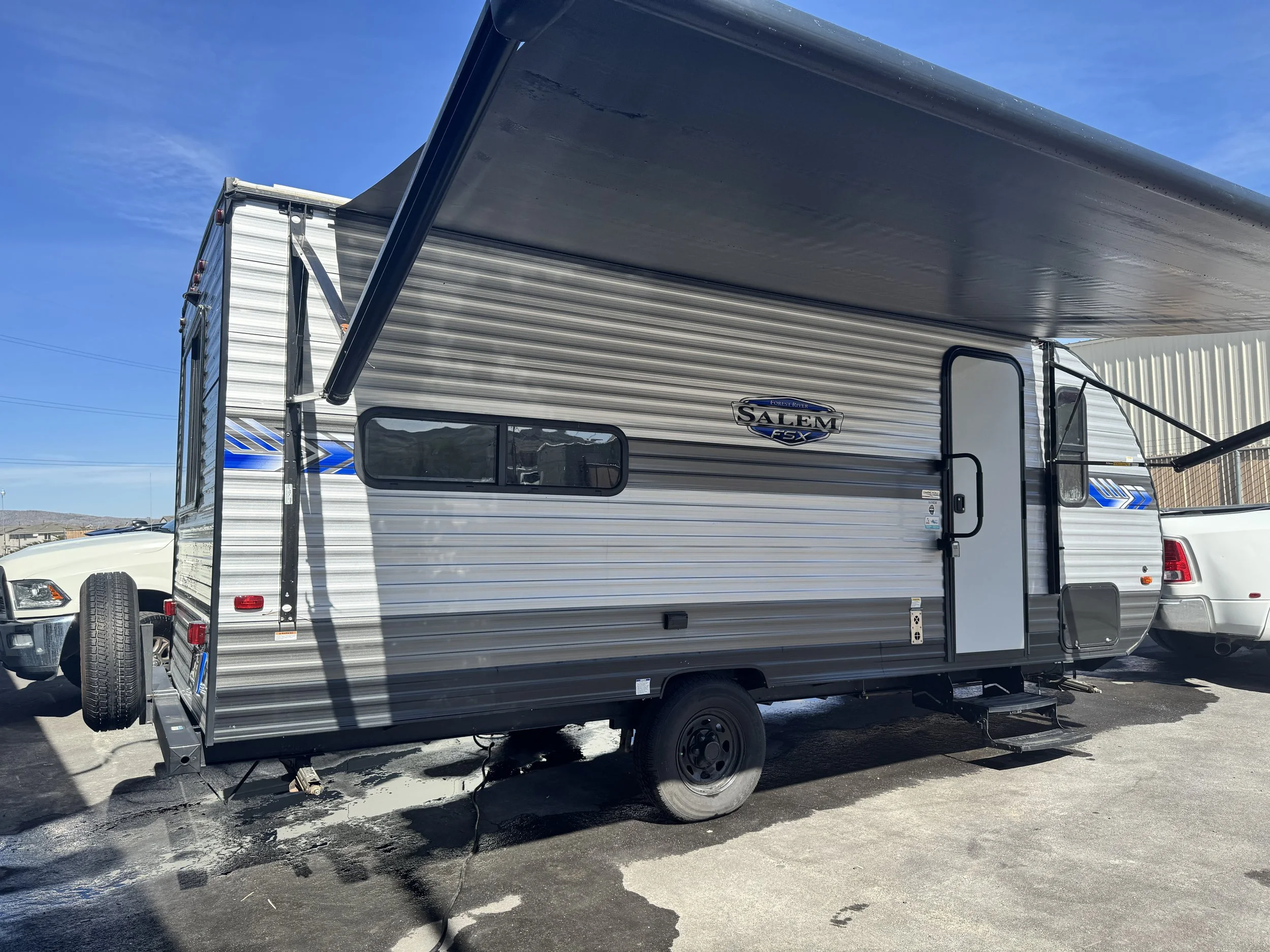 A silver Salem FTX travel trailer with an extended awning parked on a paved lot under a clear blue sky.