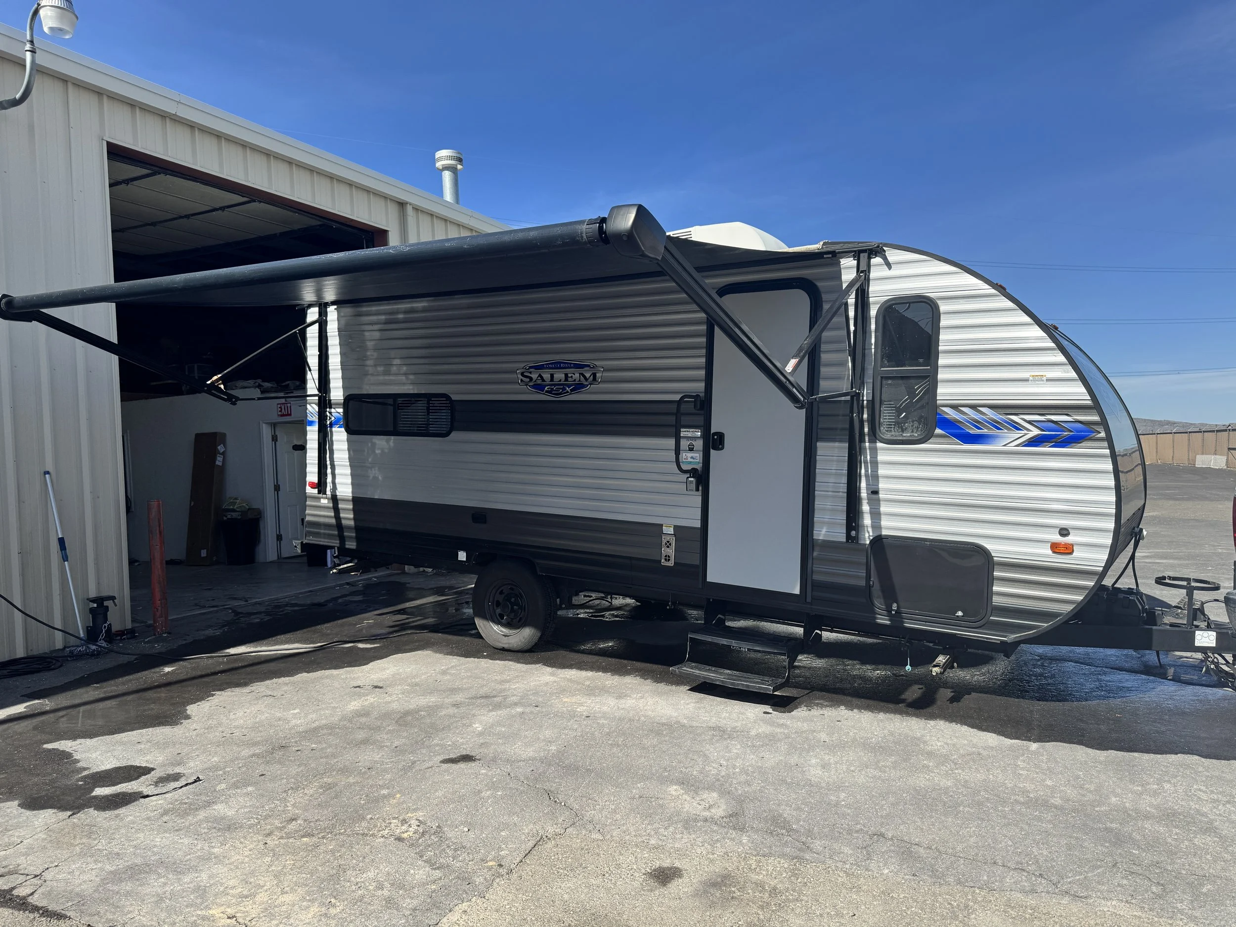 A travel trailer parked outside a building with a partially open garage door, under a clear blue sky.