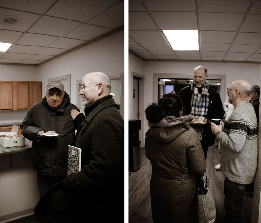 People gathered indoors at a social event, some holding coffee cups and snacks, engaged in conversation.