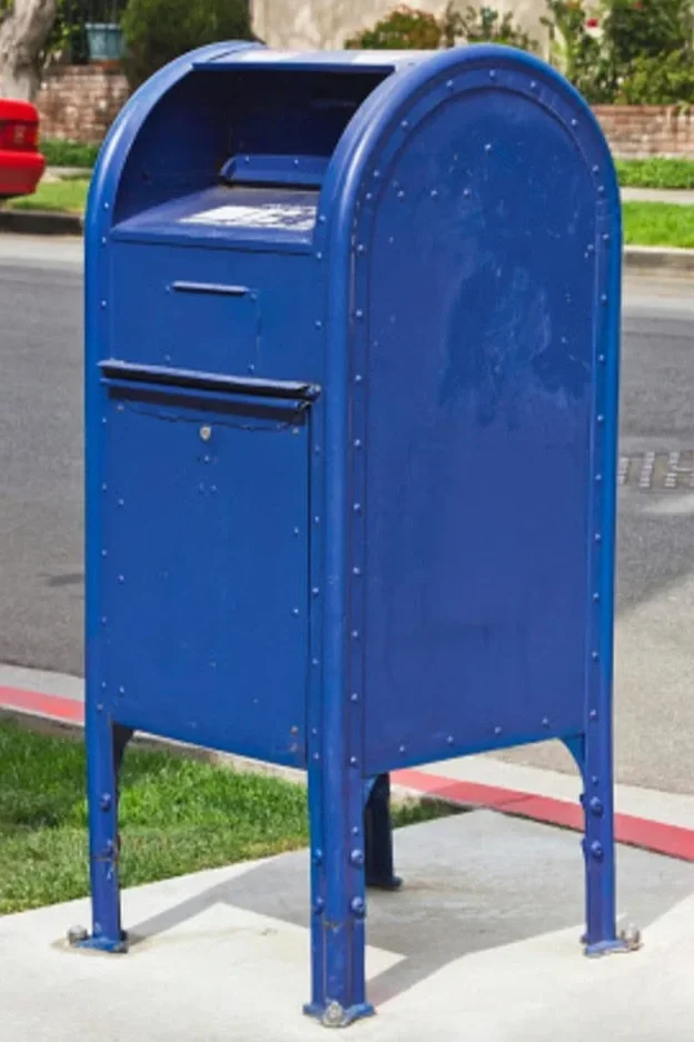 Blue public mailbox on sidewalk in residential neighborhood.