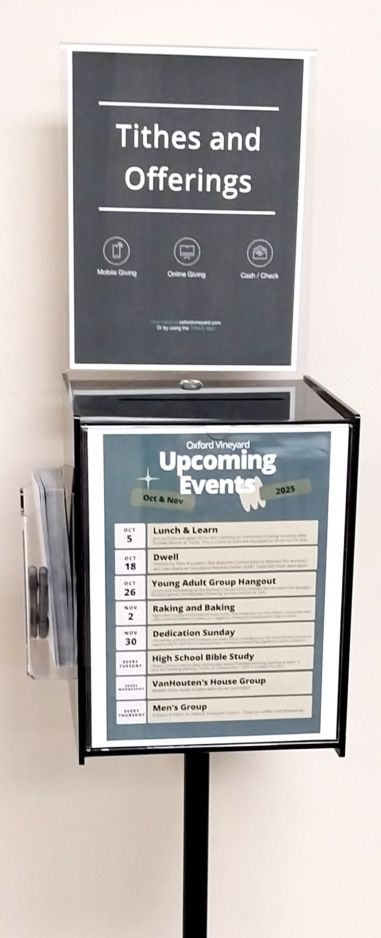 Signboard displaying upcoming events at Oxford Vineyard, including Lunch & Learn, Dwell, Young Adult Group Hangout, Raking and Baking, Dedication Sunday, High School Bible Study, VanHouten's House Group, and Men's Group, with dates in October and November 2025.