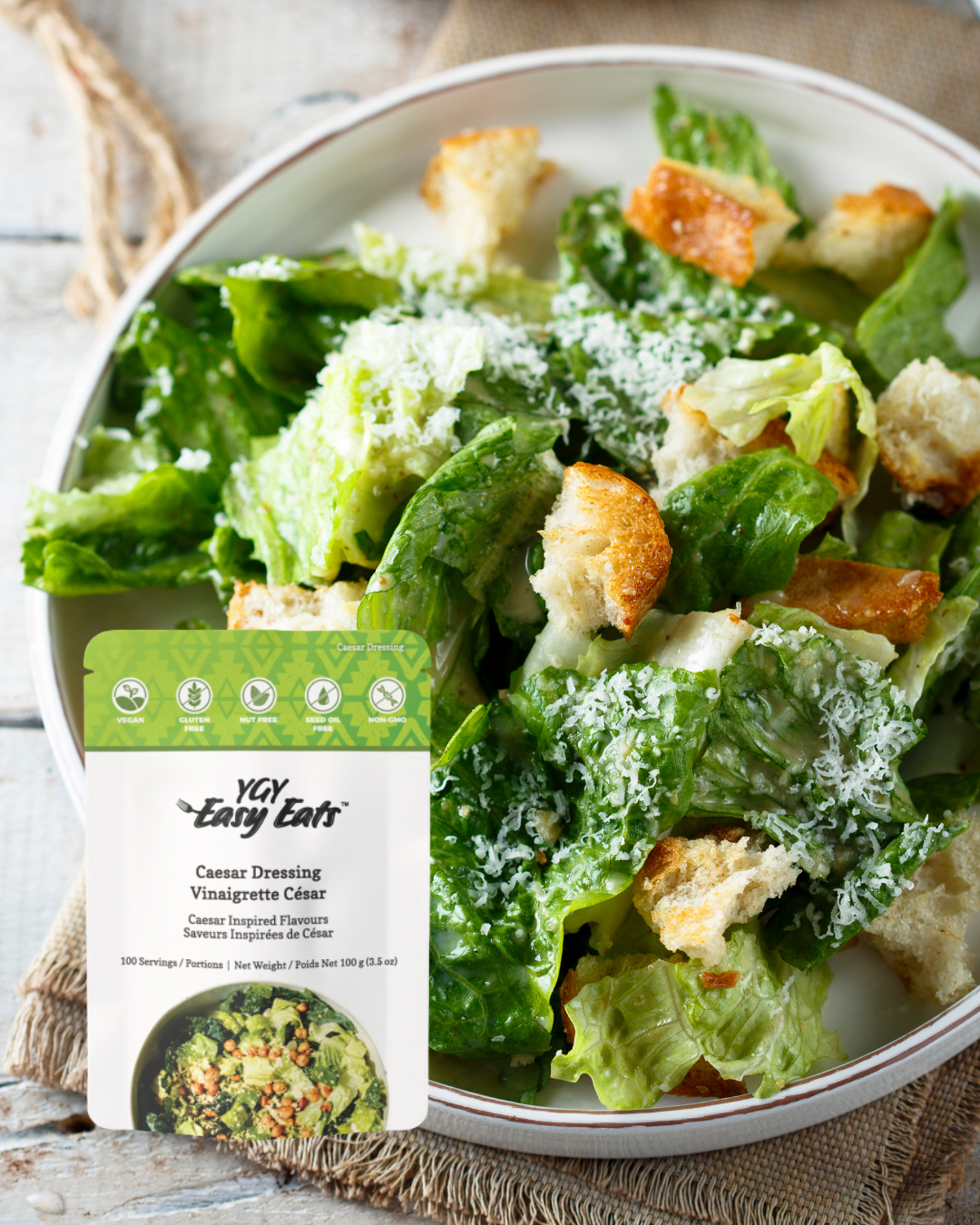 Fresh Caesar salad with Romaine lettuce, croutons, and grated cheese in a white bowl, with a packet of YGY Easy Eats Caesar Dressing on the side.