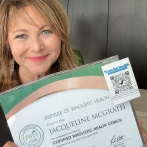 A woman with blonde hair and blue eyes holding a certificate from the Institute of Wholistic Health, recognizing her as a certified wholistic health coach.