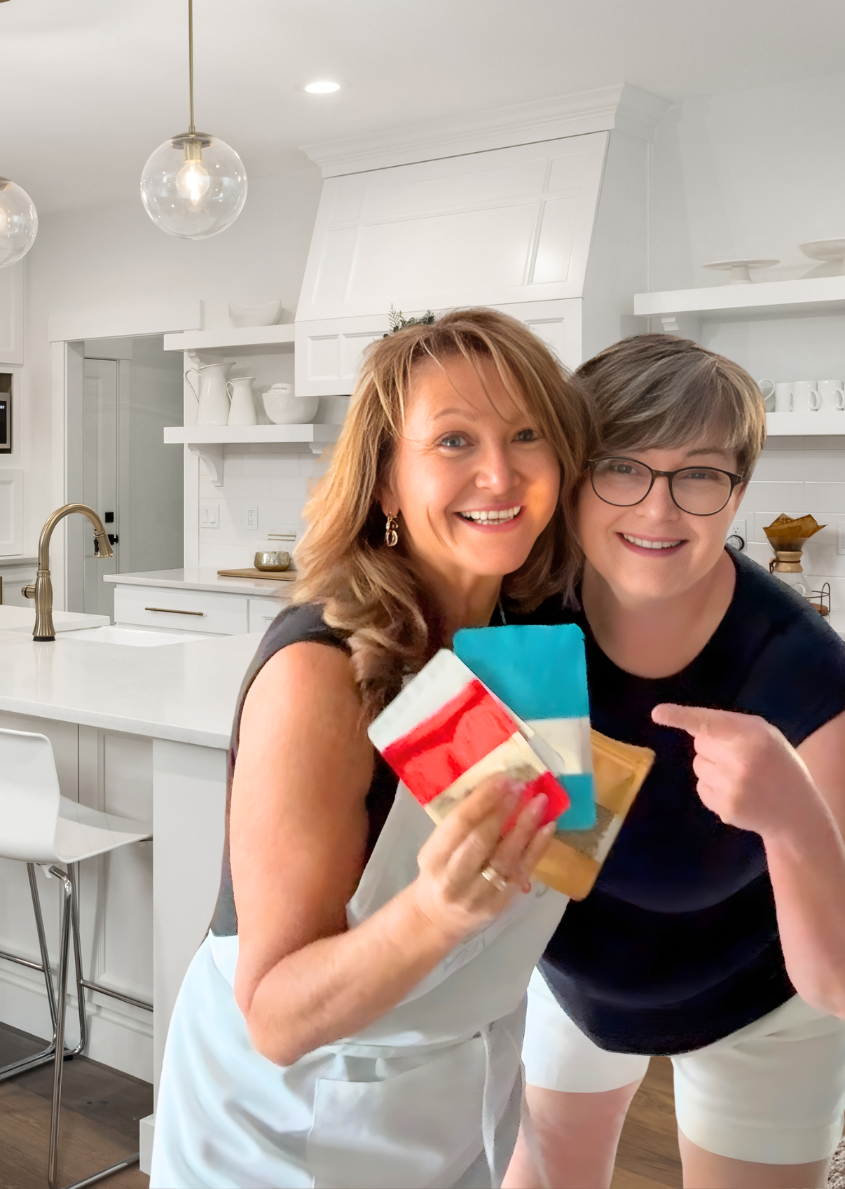 Two women smiling and holding cookies in a bright white kitchen with modern decor.