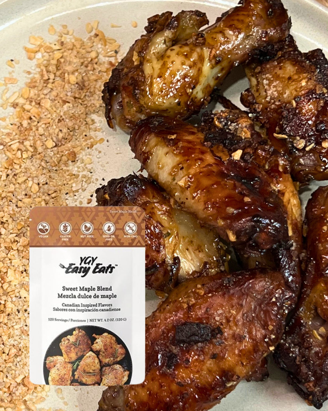 Cooked chicken drumsticks with glazed, caramelized surface next to a package of Yay Easy Eats Sweet Maple Blend seasoning, with a background of crushed nuts or grains.