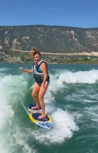 Woman surfing on a wave in a large body of water with mountains in the background. Jacqueline McGrath
