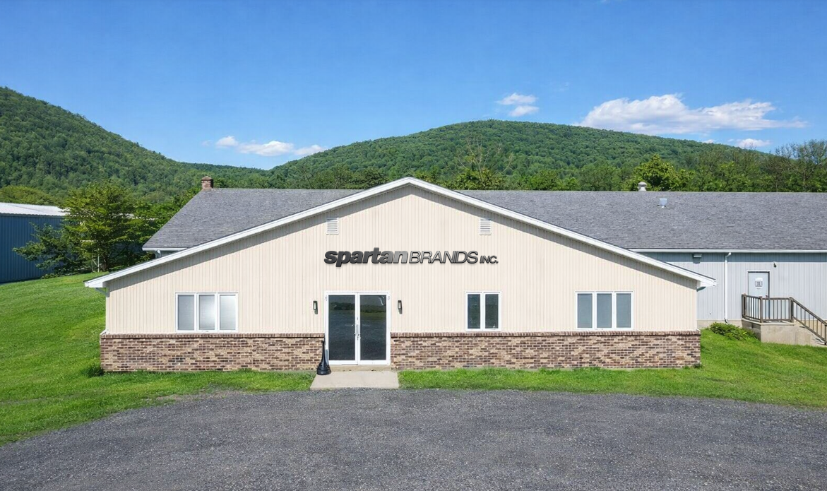 Beige and brick Spartan Brands Inc building with green mountains in the background