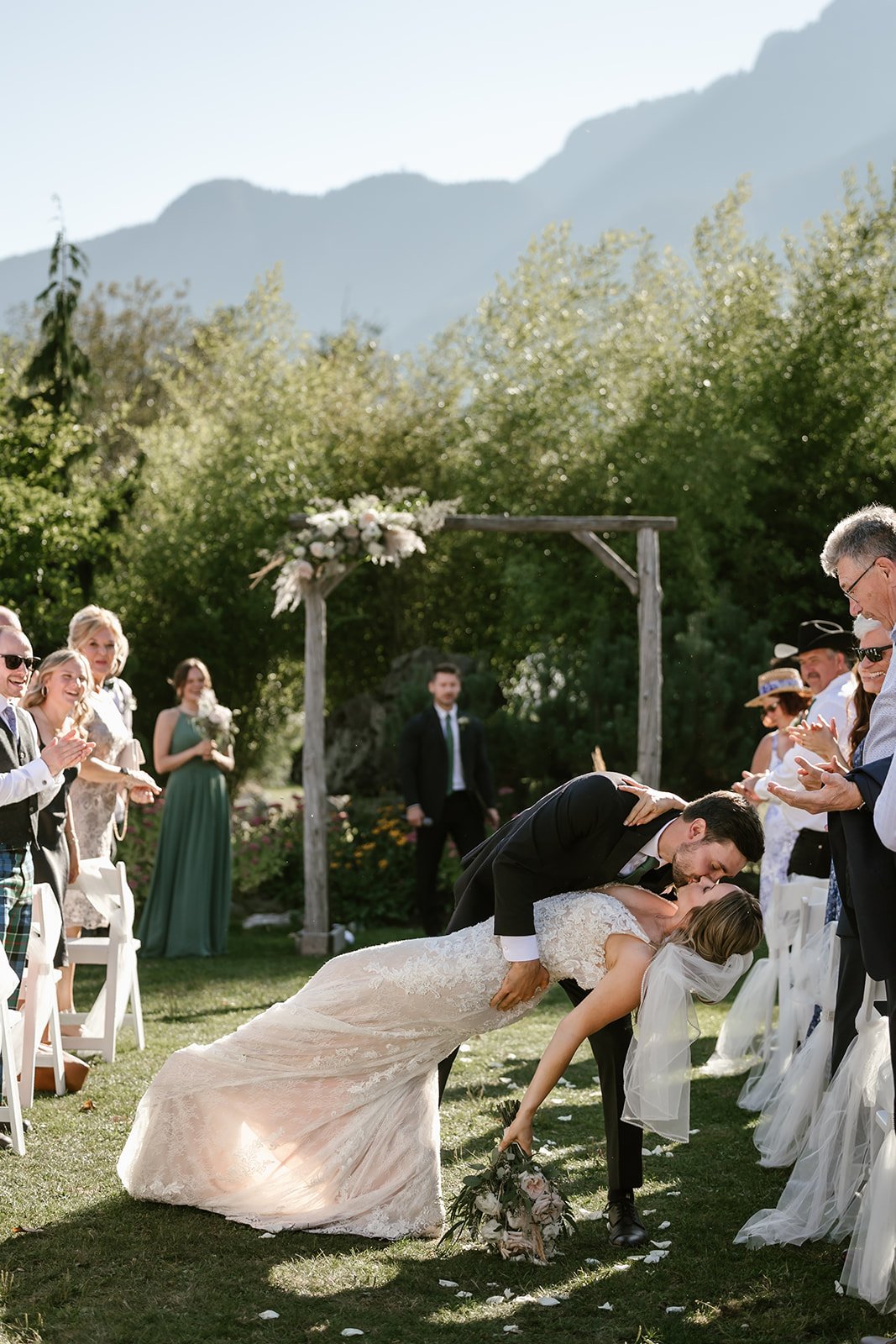  A groom dipping a bride in an aisle with wedding guests on either side, and mountains behind them.  