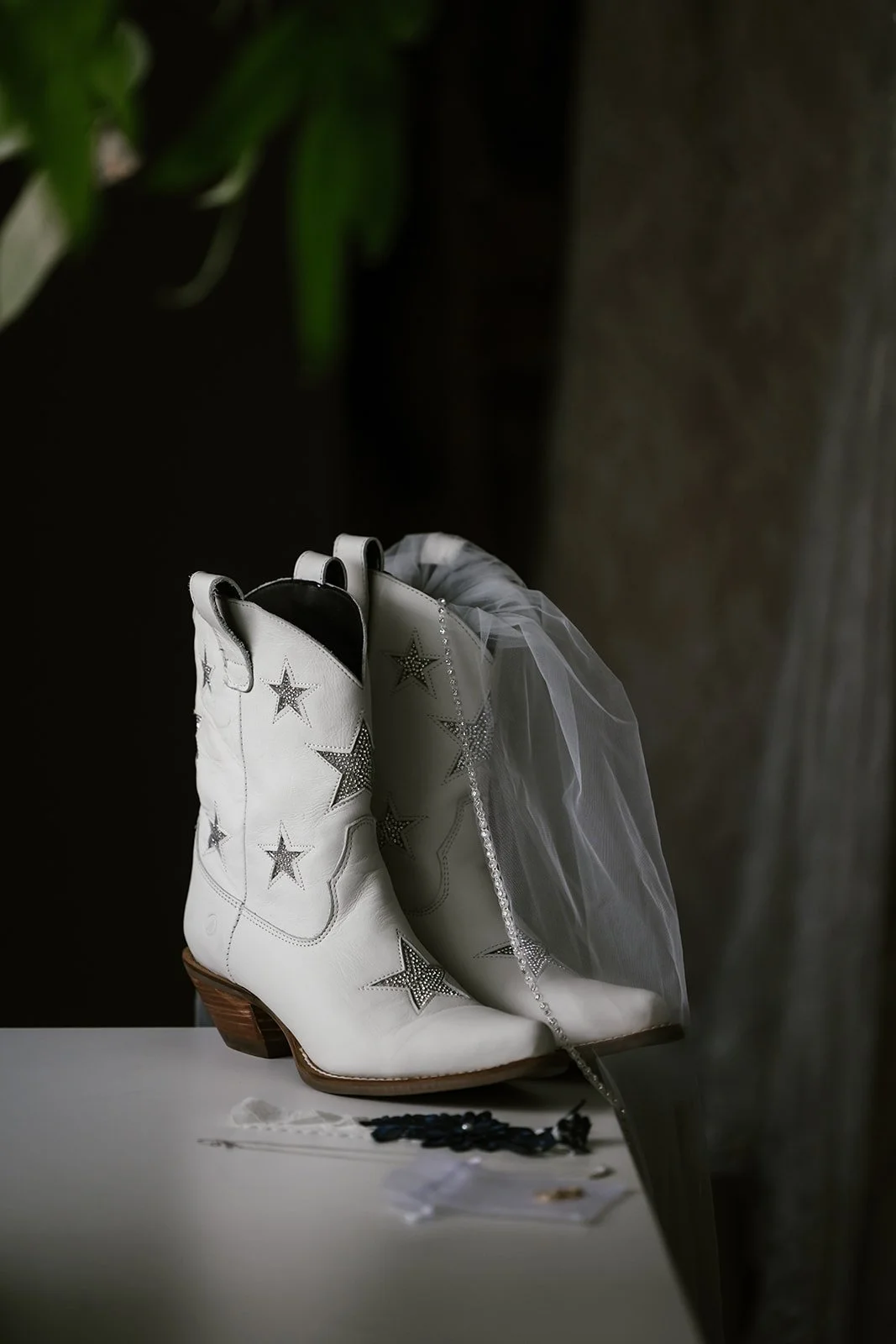  A pair of white cowboy boots with a veil on a table.  